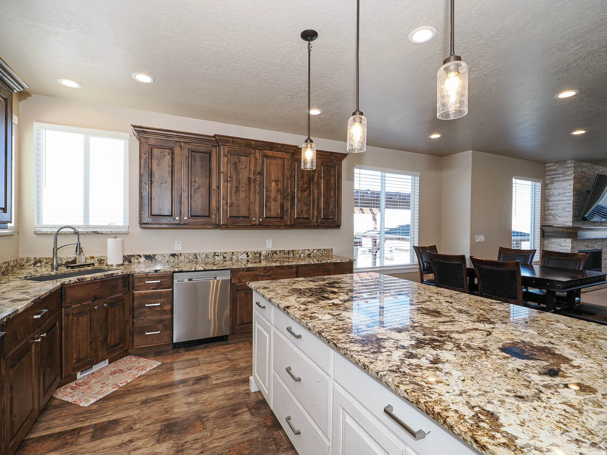 Two tone kitchen featuring dual tone cabinetry, light stone countertops, dishwasher, decorative light fixtures, and dark wood-style floors