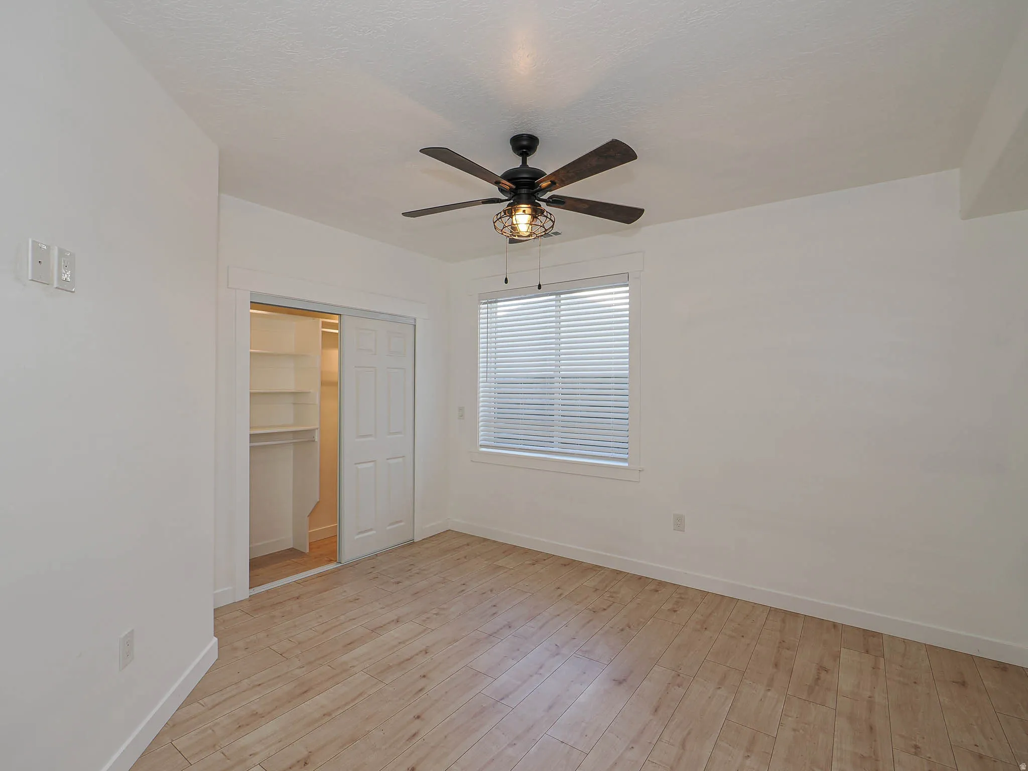 Unfurnished bedroom featuring light wood-style floors, a spacious closet, and a ceiling fan