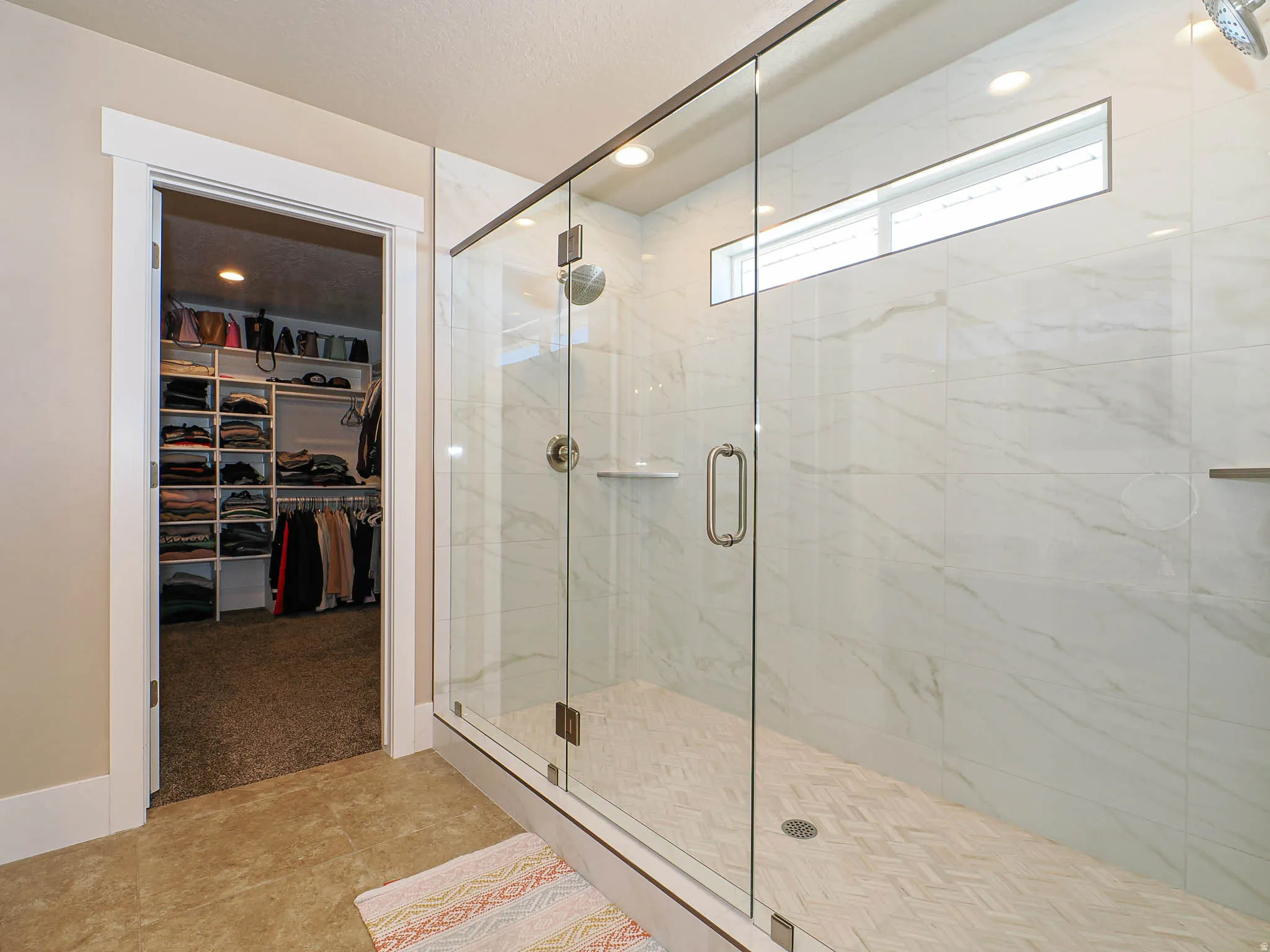 Full bath featuring a spacious closet, a marble finish shower, light colored carpet, and light tile patterned flooring