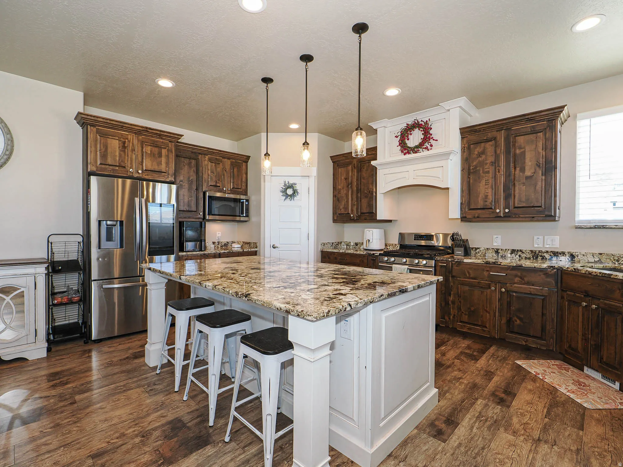 Dual tone kitchen with stainless steel appliances, a breakfast bar, light stone counters, pendant lighting, and dark wood-style flooring
