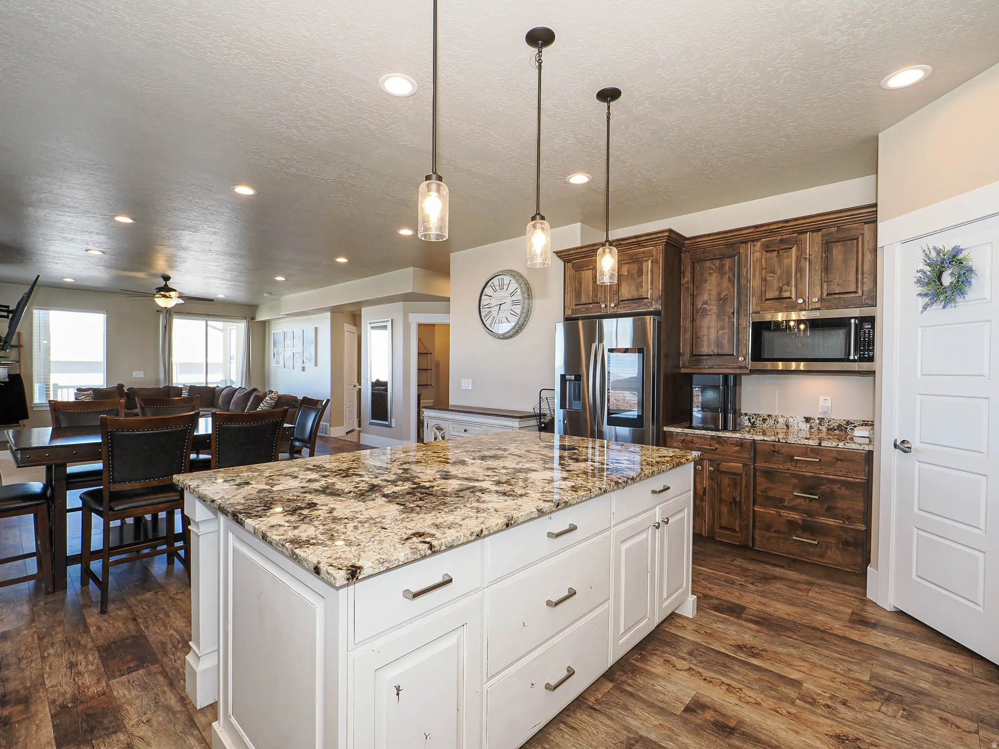 Kitchen with dual tone cabinetry, stainless steel appliances, light stone counters, open floor plan, and dark wood-style flooring