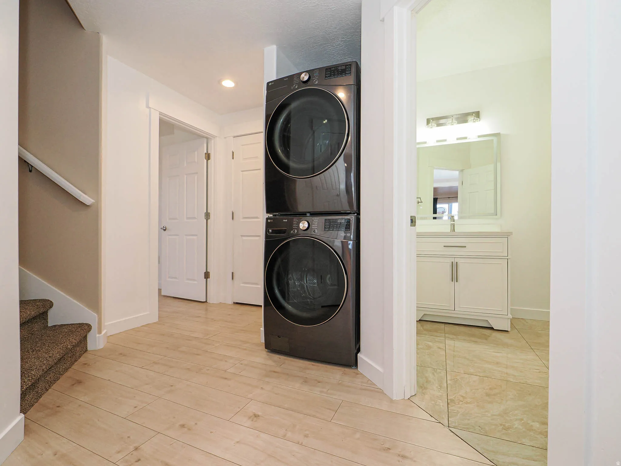 Laundry area featuring stacked washer and clothes dryer, light wood-style flooring, and recessed lighting