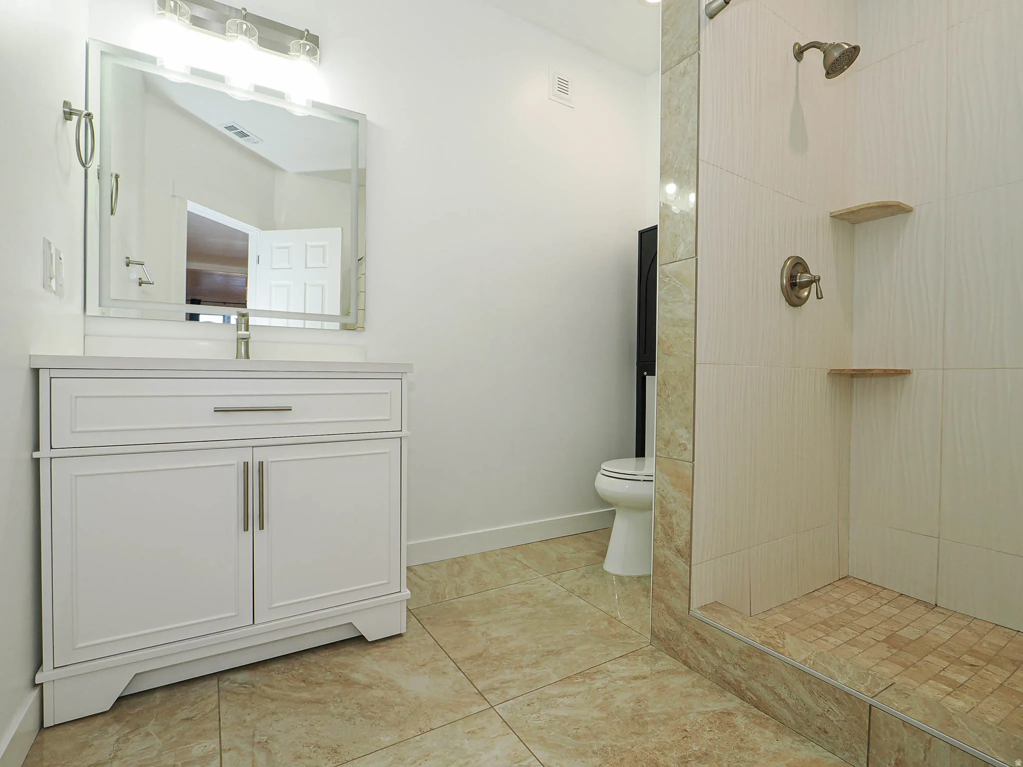 Bathroom featuring vanity, tiled shower, and light tile patterned floors