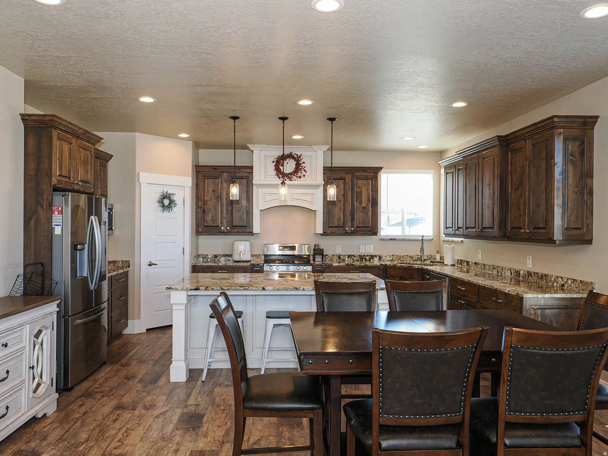Kitchen featuring dark stone counters, dark wood finish cabinetry, stainless steel appliances, pendant lighting, and a textured ceiling