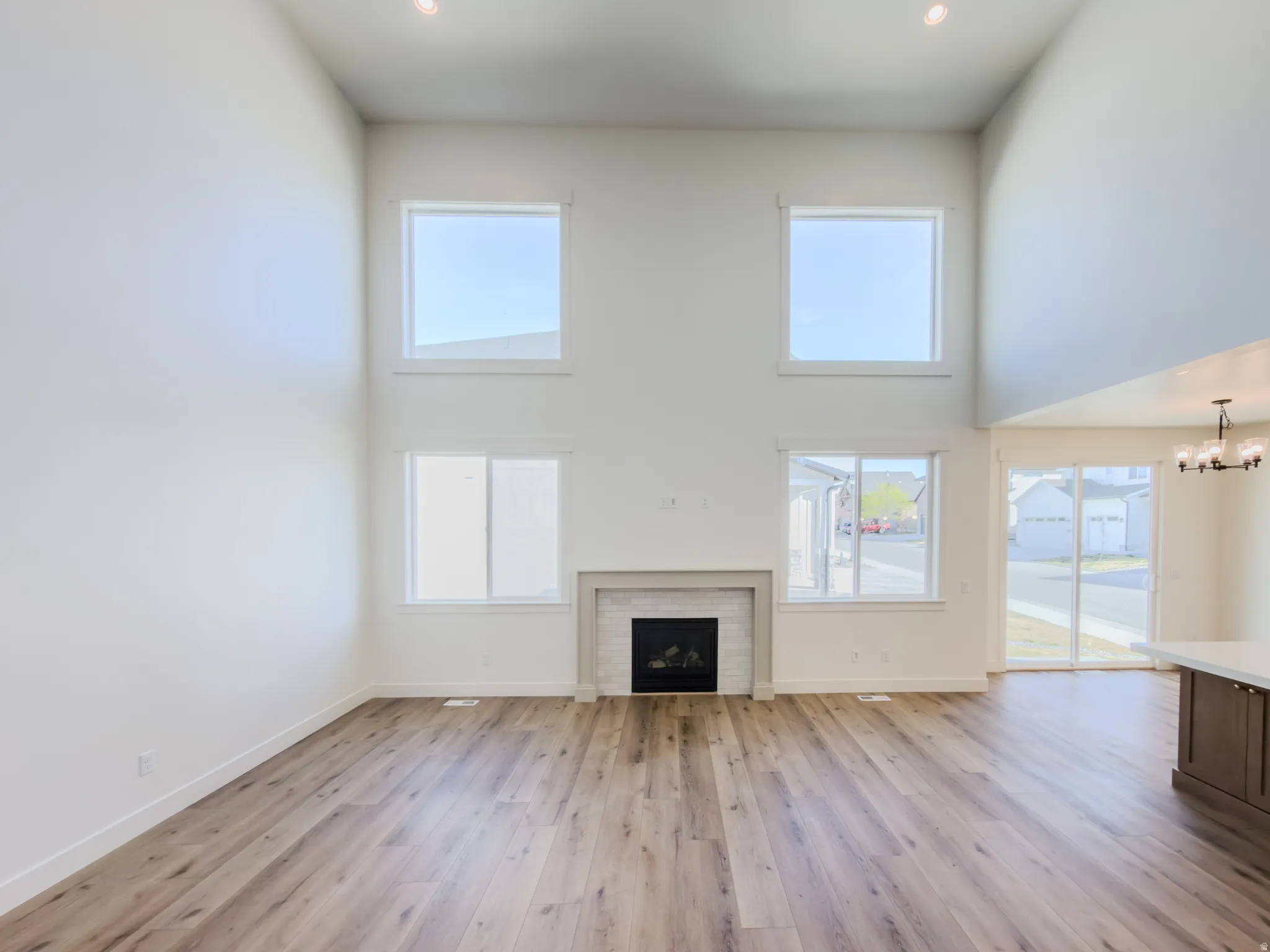 Unfurnished living room with a high ceiling, a fireplace, light wood-style floors, and suspended lighting