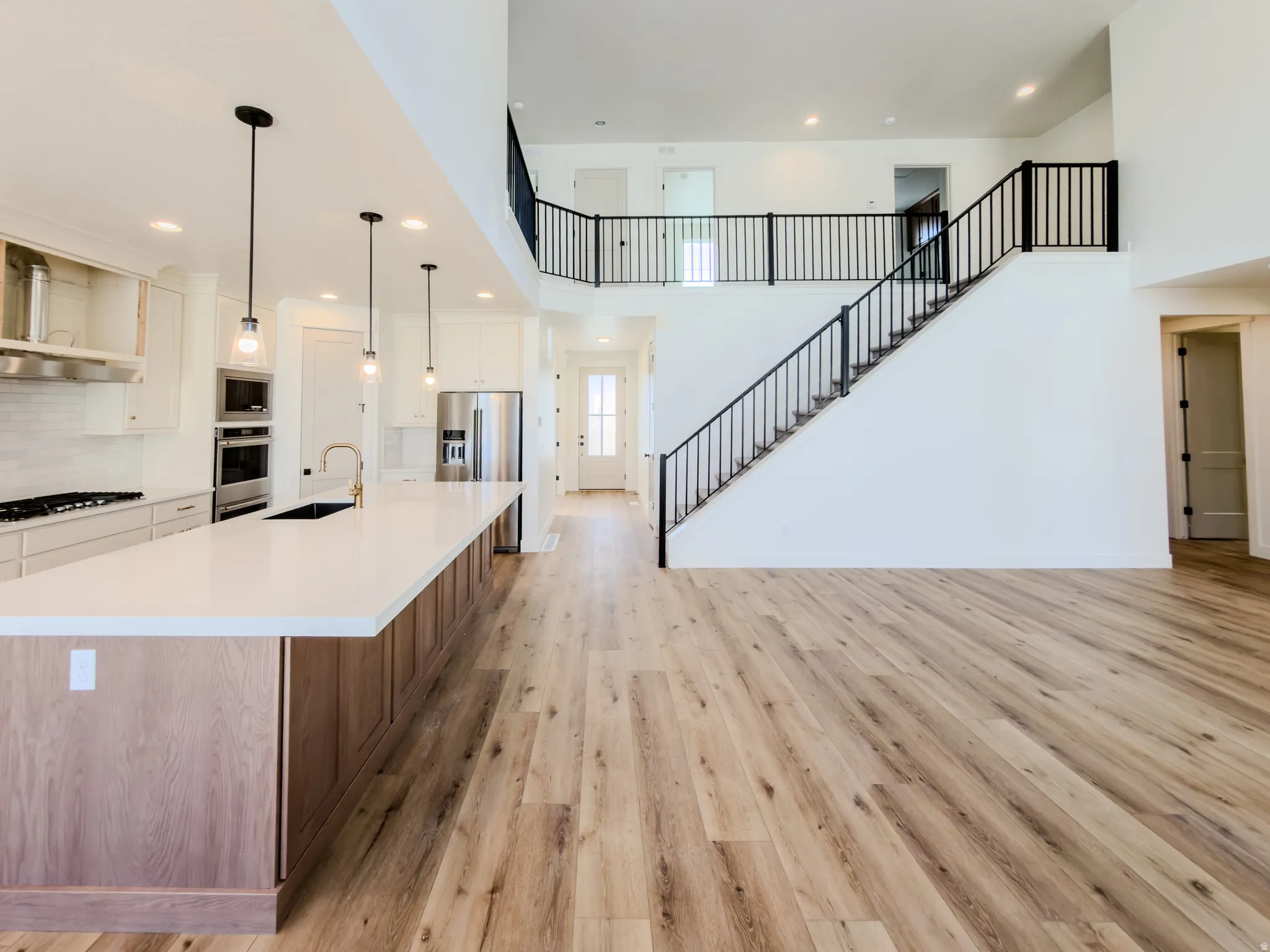 Kitchen with two tone color scheme, a large island with sink, light wood finished floors, hanging light fixtures, and a high ceiling
