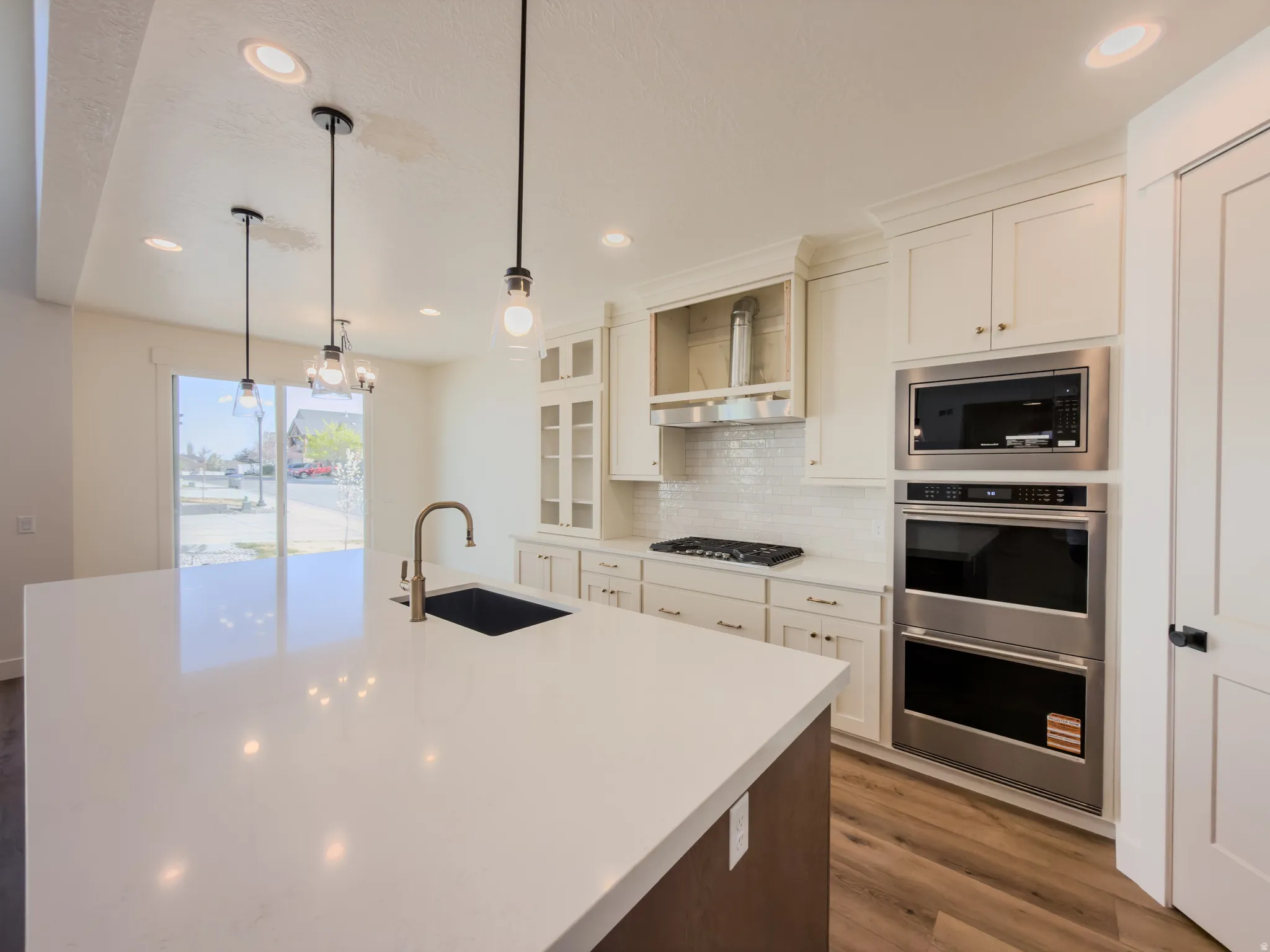 Kitchen featuring stainless steel appliances, dark wood finished floors, a kitchen island with sink, light stone countertops, and backsplash