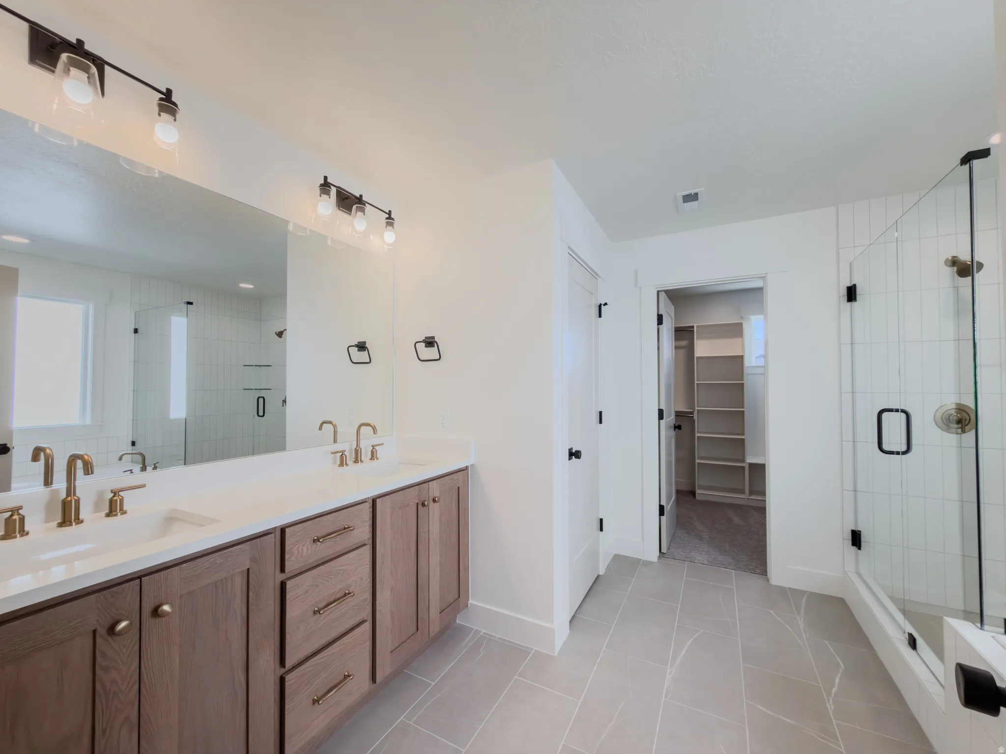 Full bath with double vanity, a shower stall, a spacious closet, and light tile patterned flooring