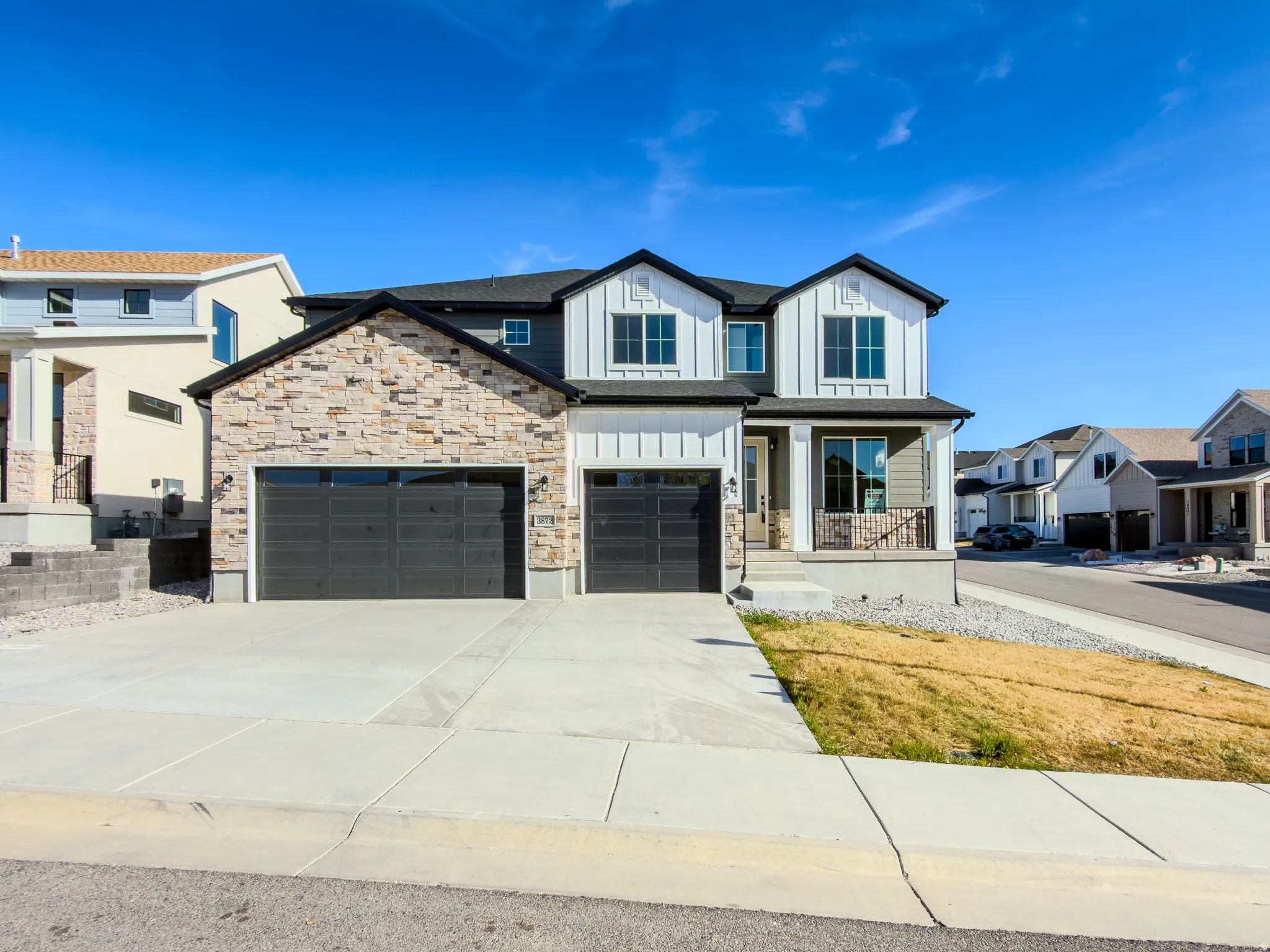 View of front of home featuring a porch, board and batten siding, concrete driveway, and stone siding