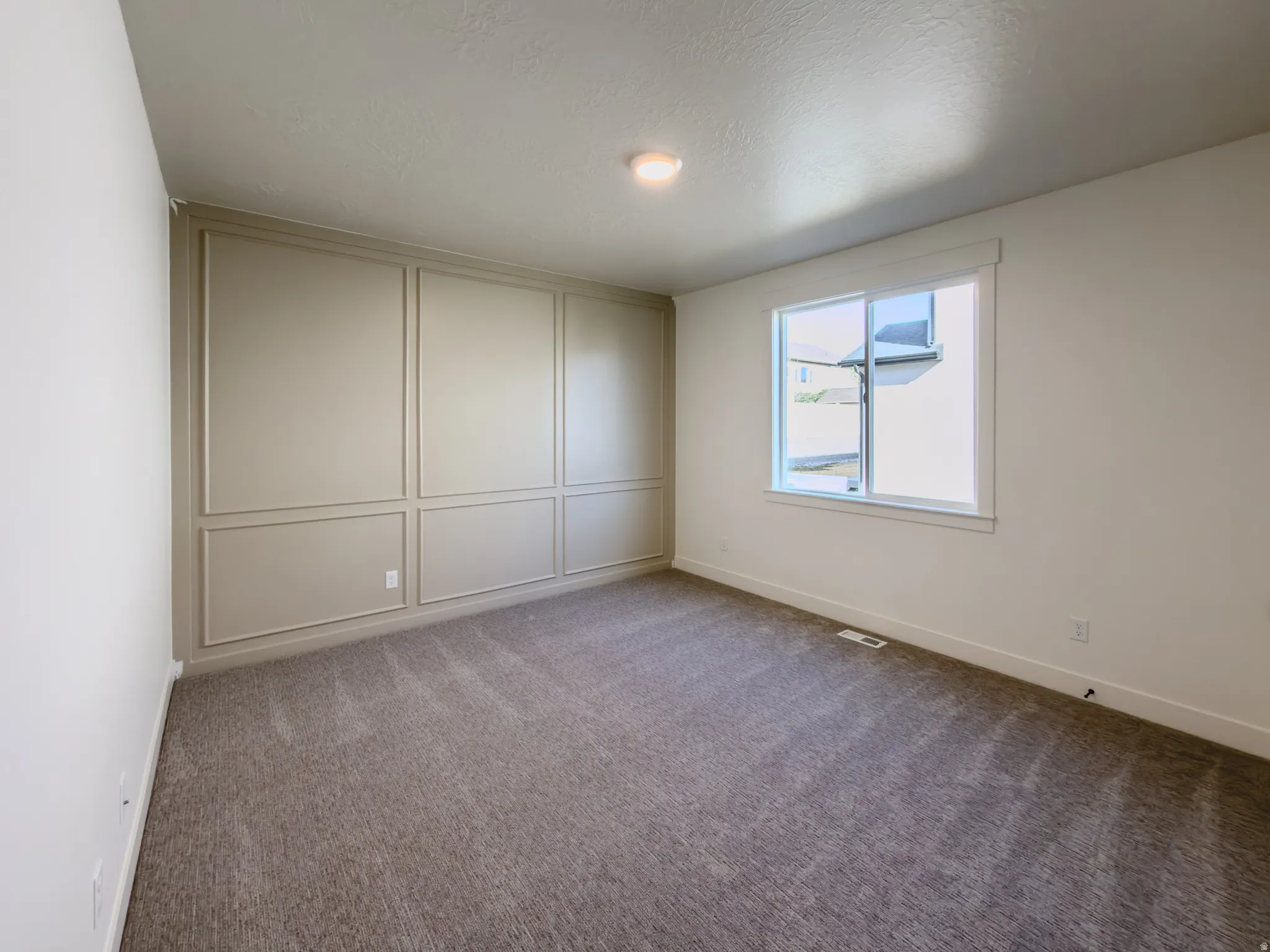Unfurnished bedroom with light carpet, a decorative wall, and a textured ceiling