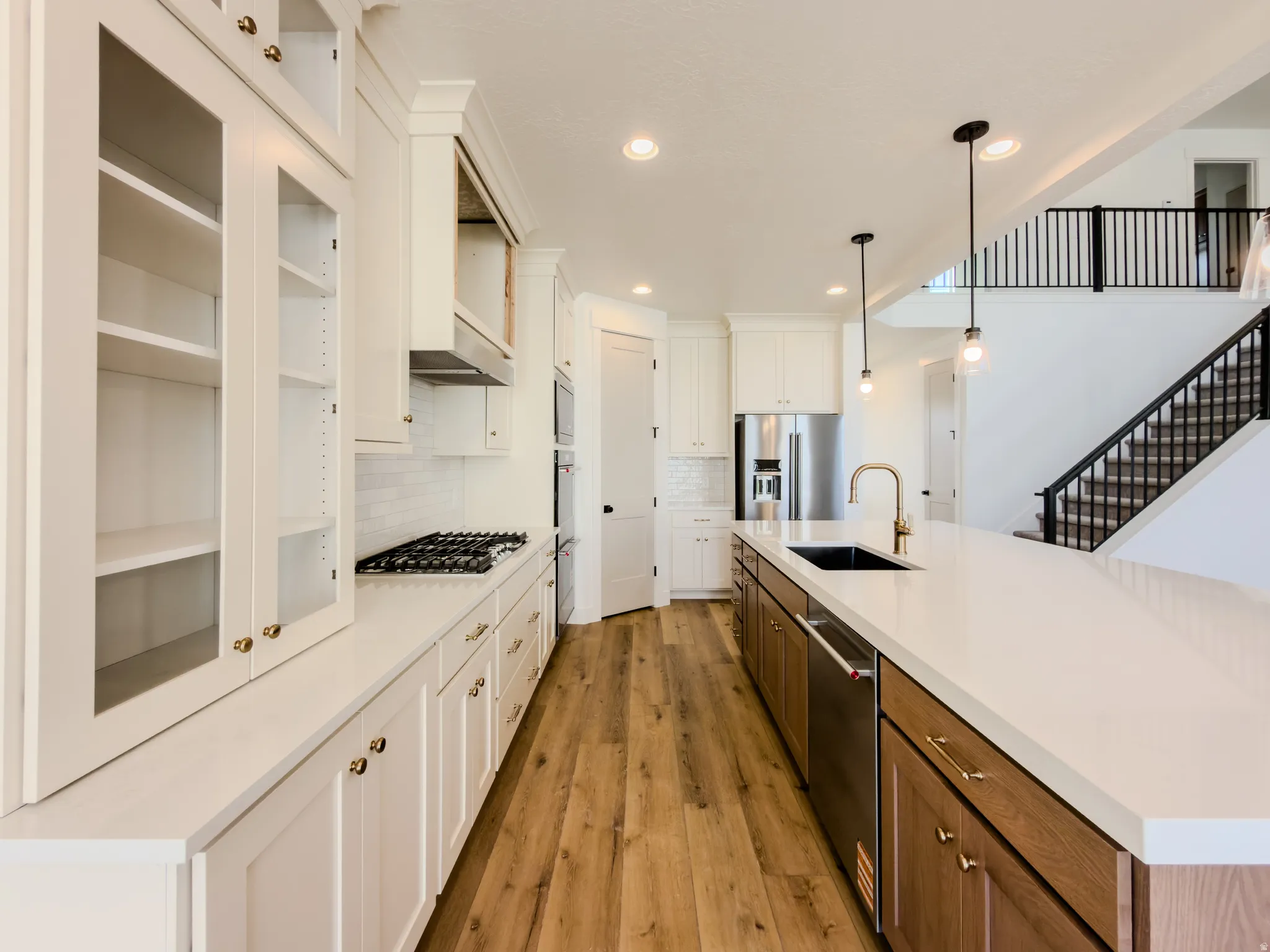 Kitchen featuring light wood-style flooring, dual tone cabinets, decorative light fixtures, stainless steel appliances, and decorative backsplash