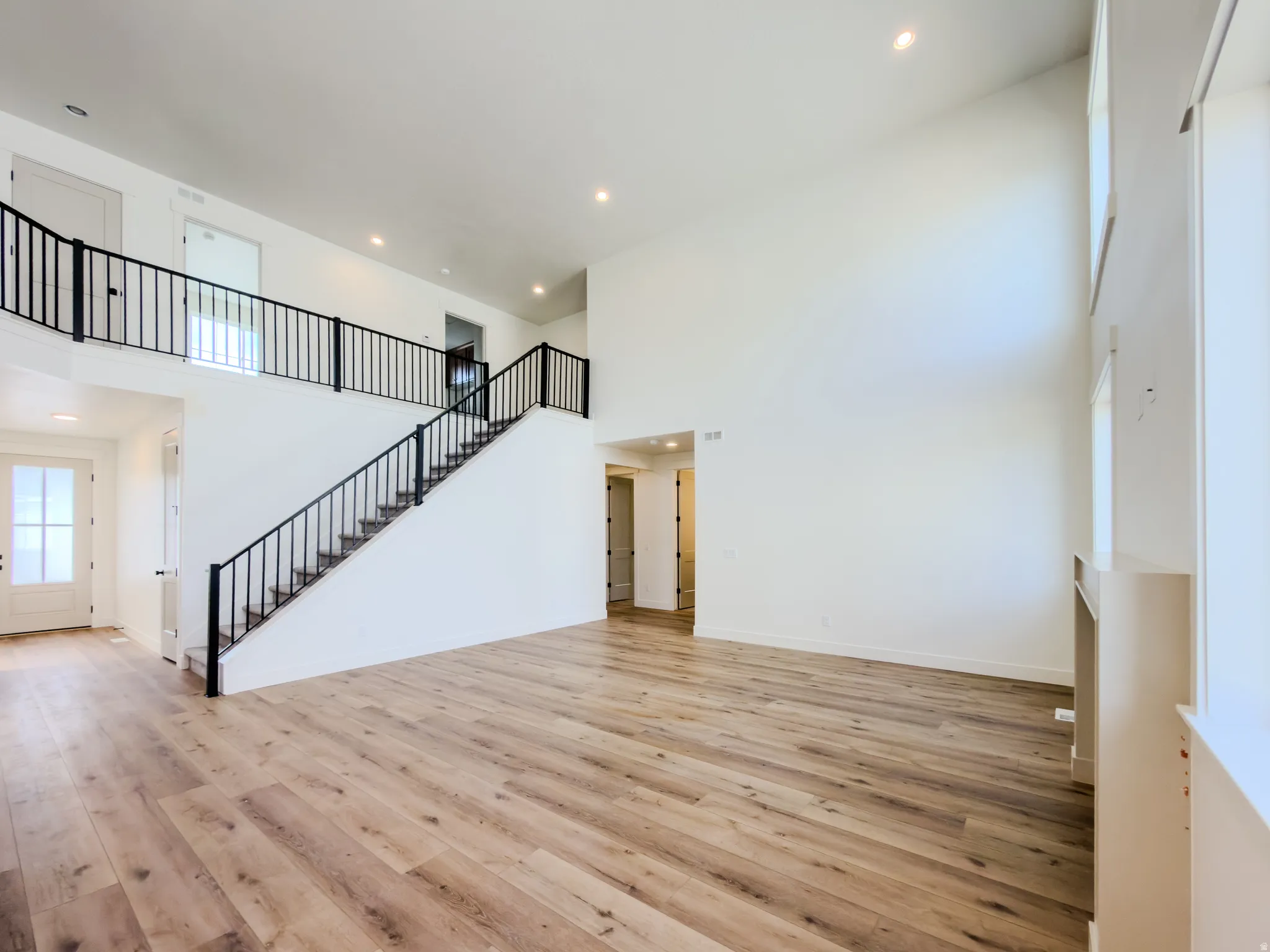 Unfurnished living room featuring a high ceiling, light wood finished floors, and recessed lighting