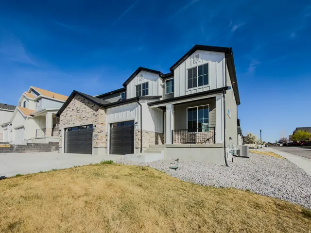 Modern farmhouse with board and batten siding, covered porch, stone siding, driveway, and a front yard