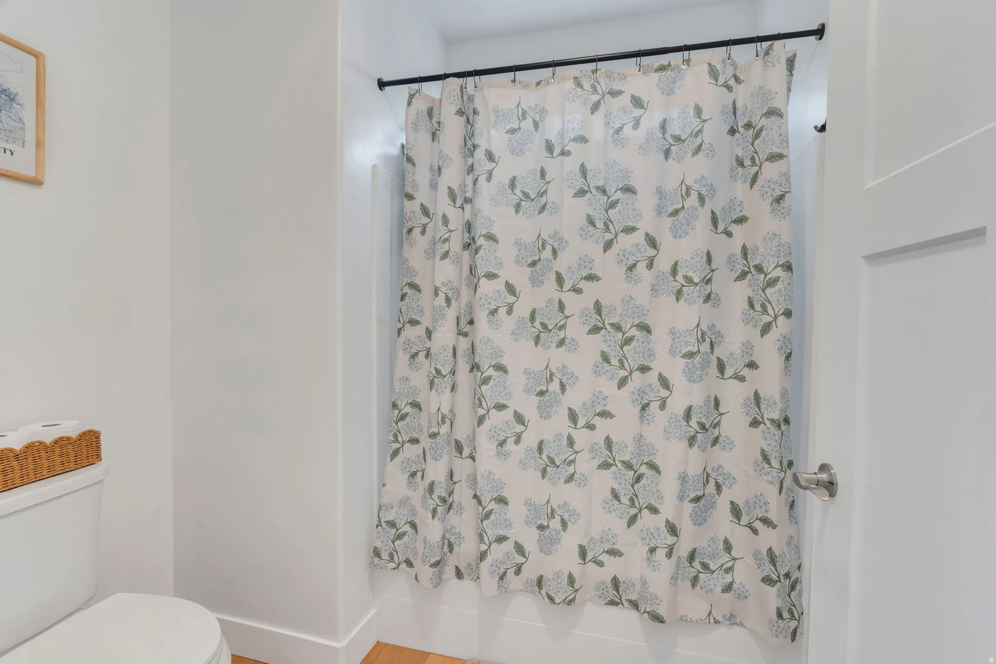 Bathroom with a shower with shower curtain and light wood-style flooring with brand new high end toilet.