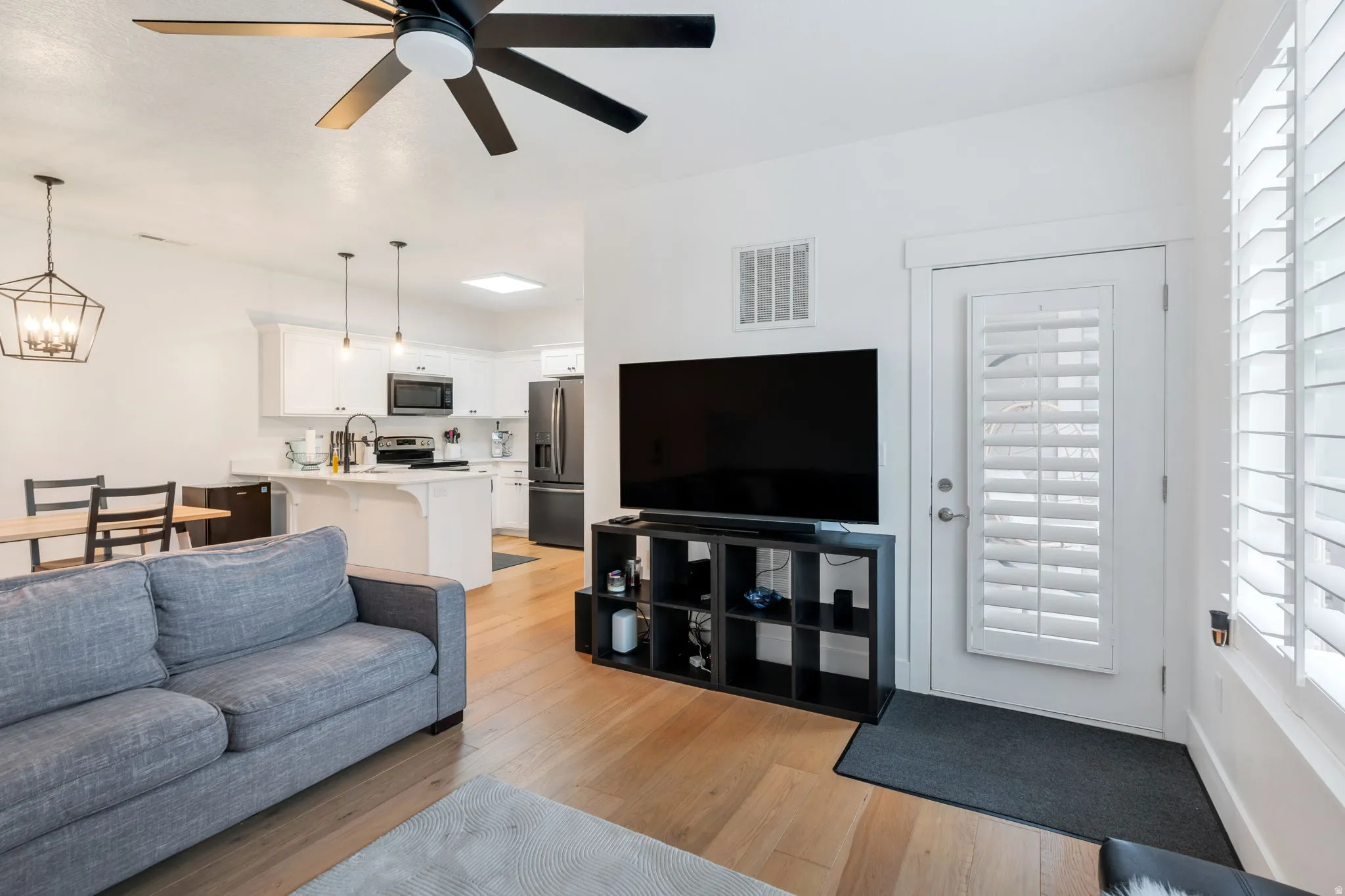 Living room with plenty of natural light, light wood finished floors, ceiling fan, and hanging lights. All furniture (table, chairs, couch, TV, Stand, etc included.