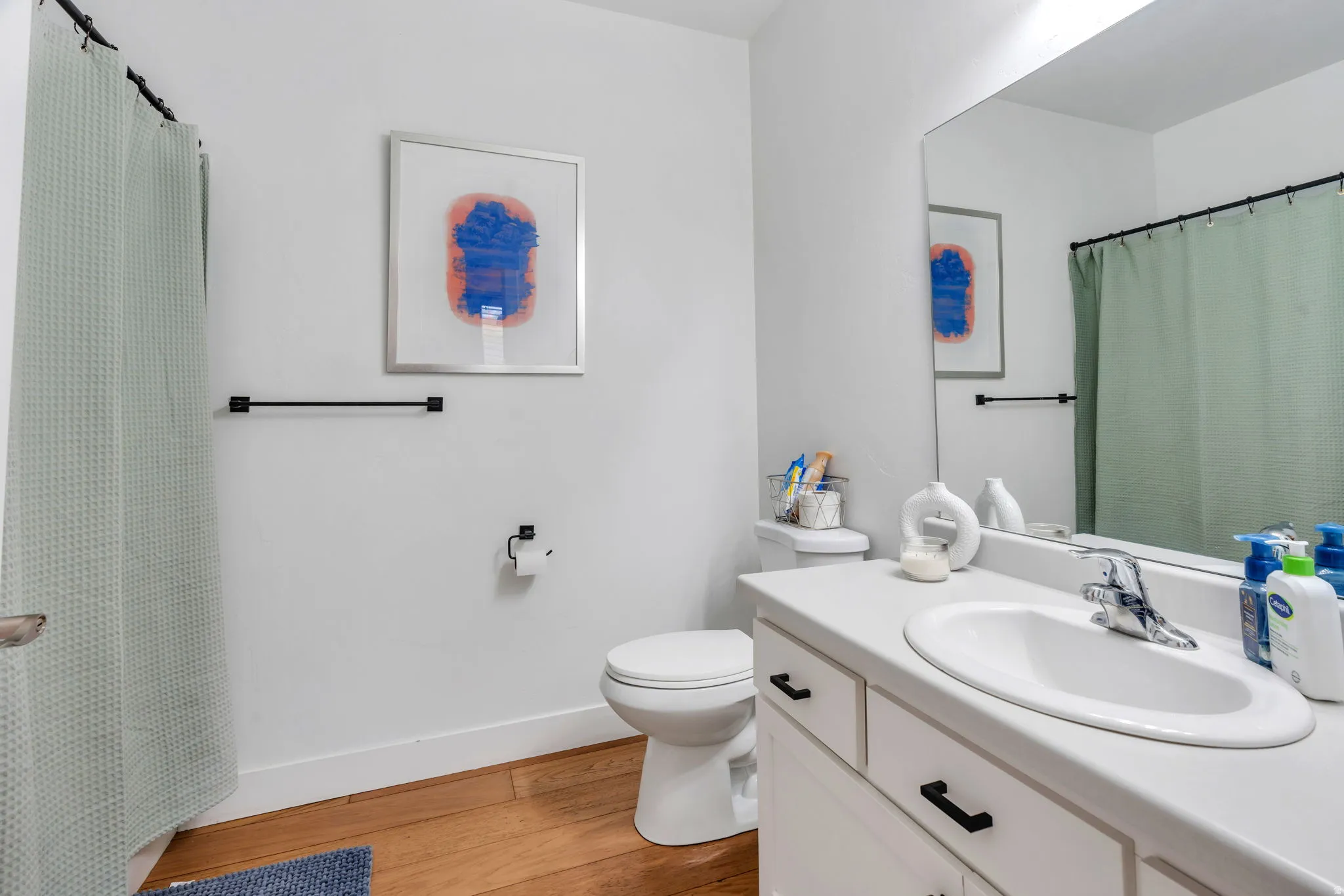Full bathroom featuring curtained shower, vanity, and light wood finished floors with brand new high end toilet.