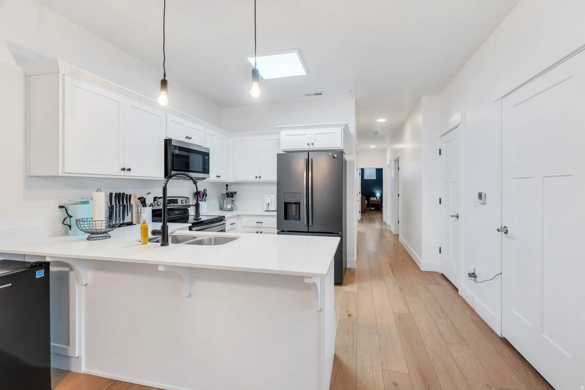 Kitchen with a peninsula, white cabinets, stainless steel appliances, a breakfast bar, and light wood-style floors