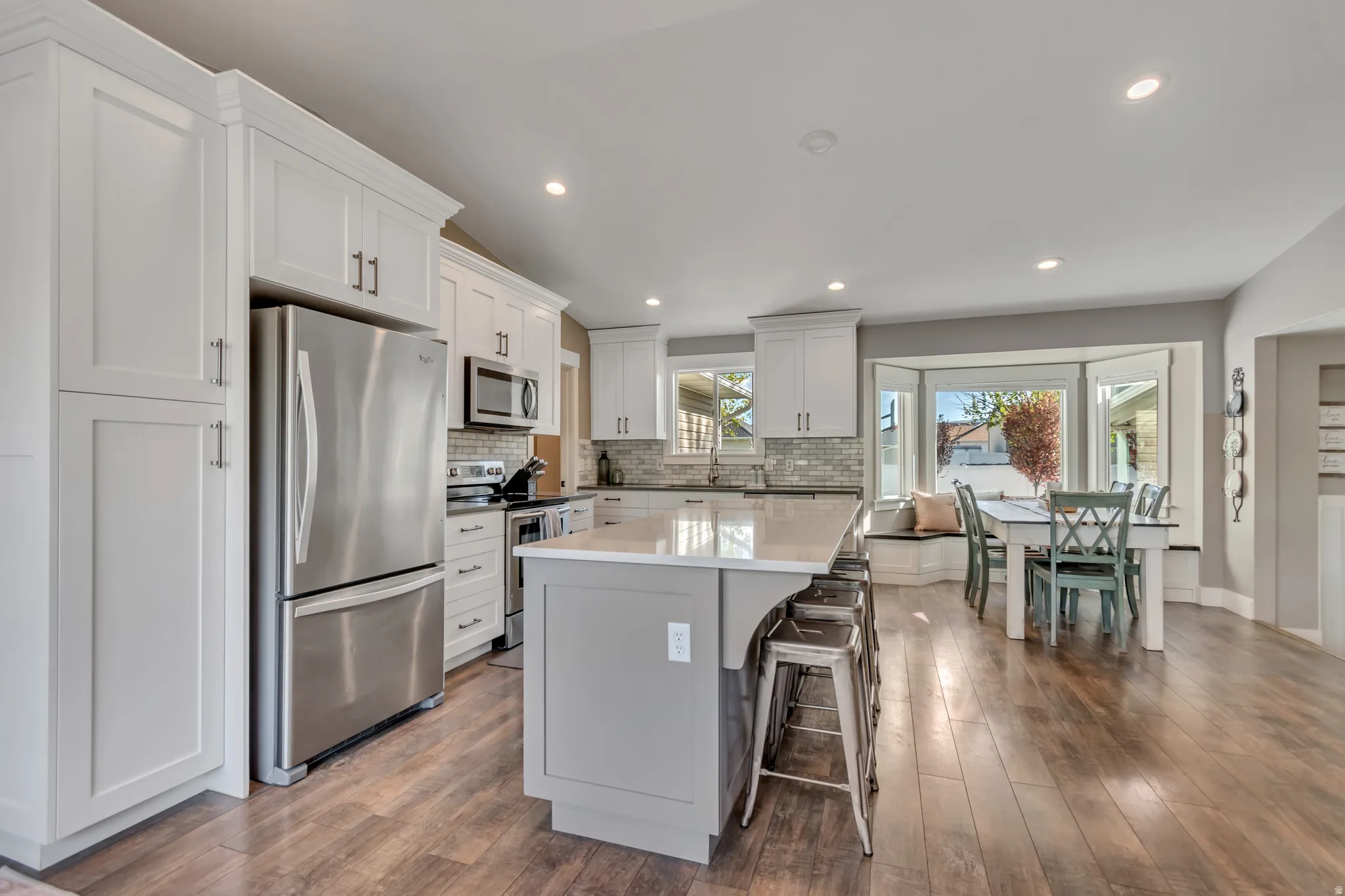 Kitchen featuring stainless steel appliances, white cabinets, dark wood-type flooring, a breakfast bar, and backsplash