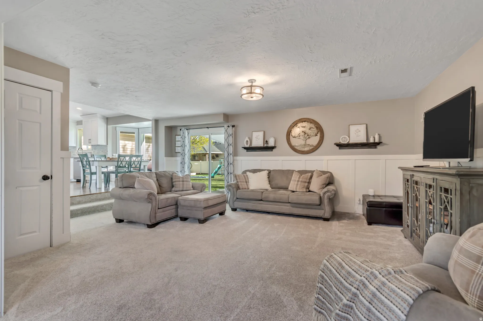 Living area with wainscoting, light carpet, a textured ceiling, and a decorative wall