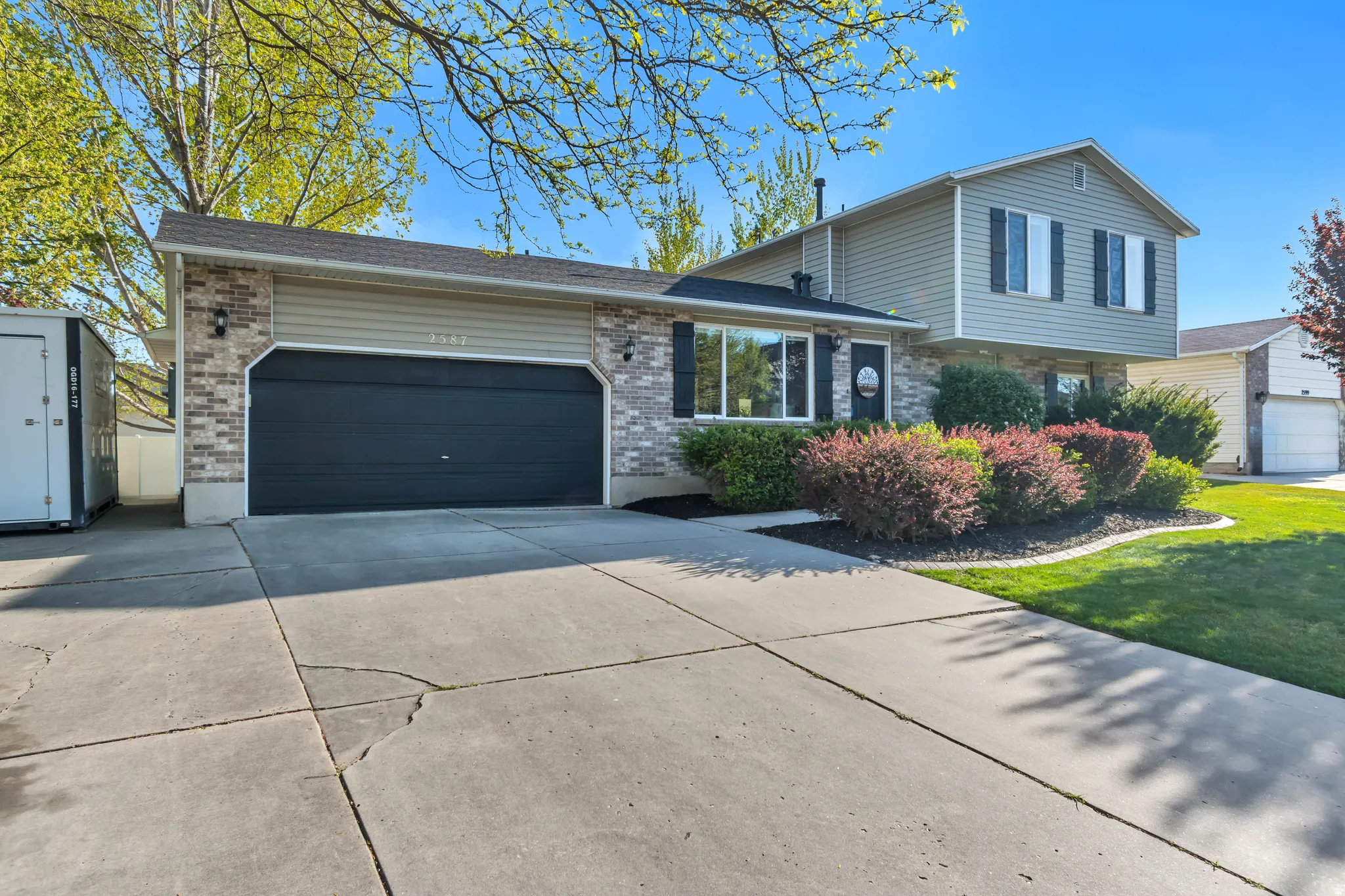 Split level home with driveway, a garage, brick siding, and a shingled roof