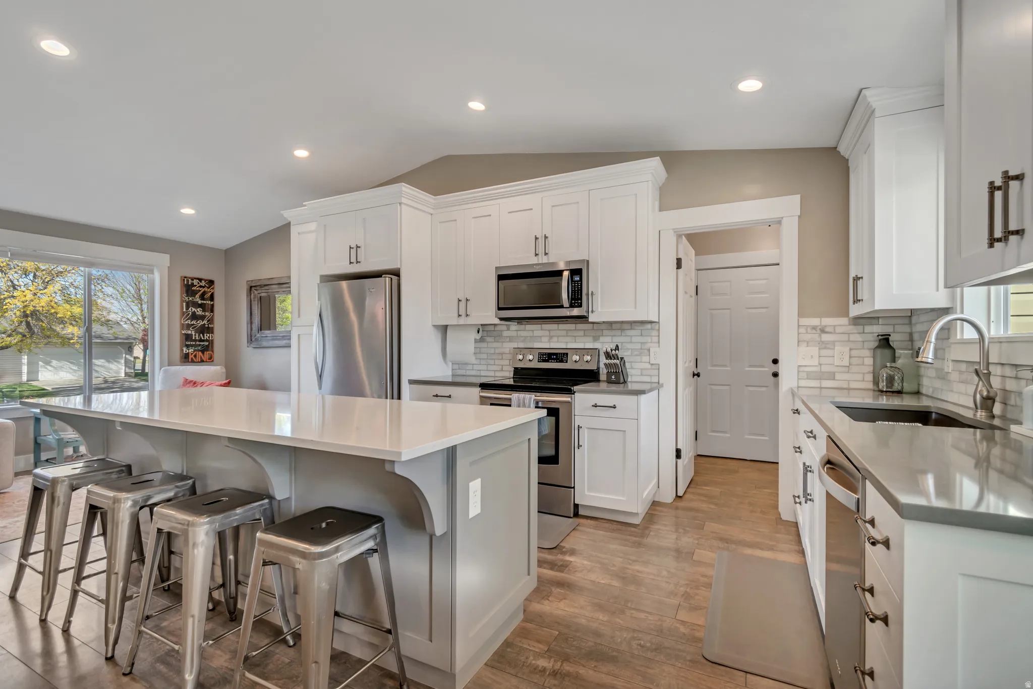 Kitchen with lofted ceiling, stainless steel appliances, a kitchen island, light wood-type flooring, and tasteful backsplash