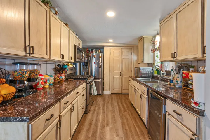 Kitchen with tasteful backsplash, light wood finish cabinetry, beverage cooler, stainless steel appliances, and light wood-type flooring