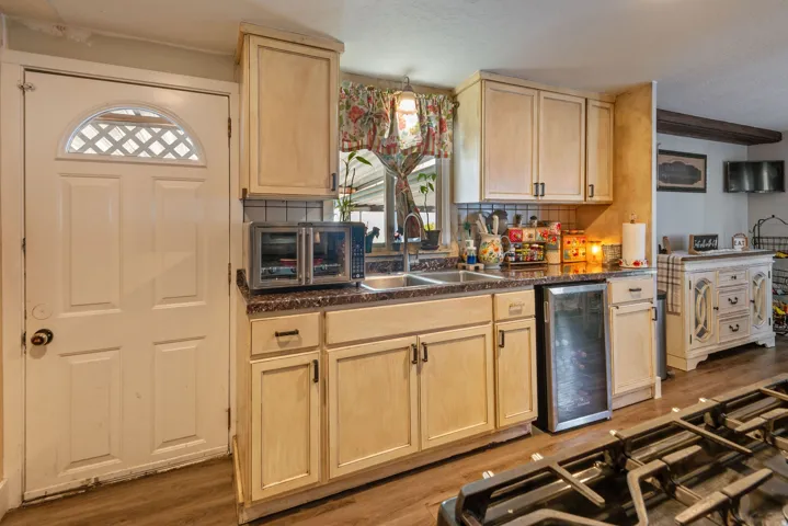 Kitchen with light wood finish cabinetry, dark countertops, tasteful backsplash, and wine cooler
