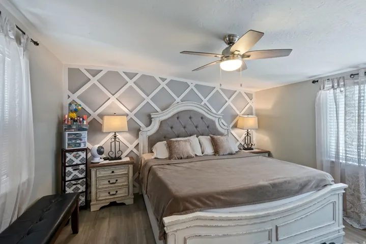Bedroom featuring ceiling fan, dark wood-style flooring, and an accent wall