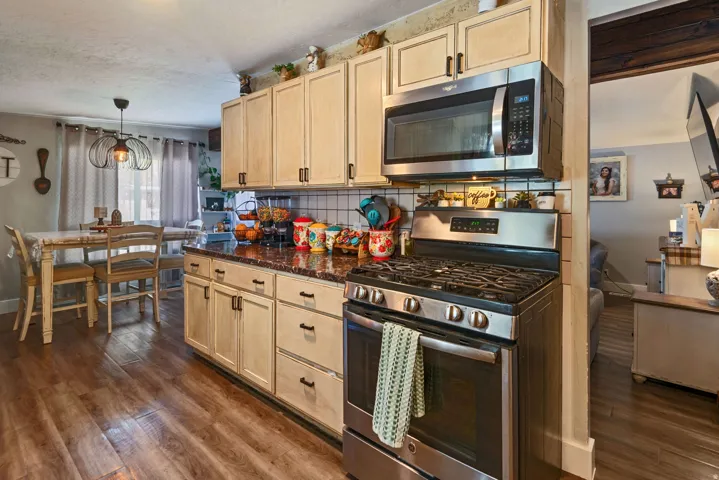 Kitchen featuring stainless steel appliances, decorative backsplash, light wood finish cabinetry, and dark wood finished floors