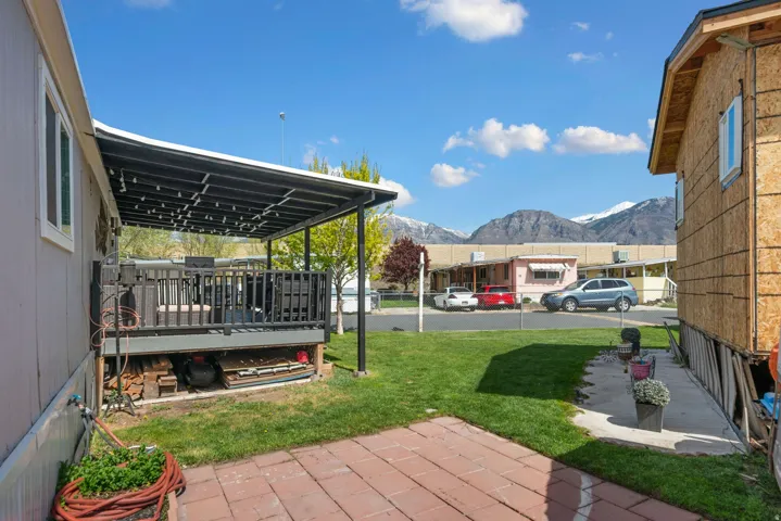 View of green lawn with a patio area and a deck with mountain view