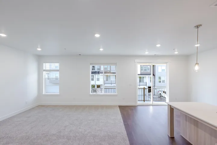 Recessed lighting, light gray carpeting, wood-finish flooring, sliding glass door, and a kitchen island with a light-toned countertop
