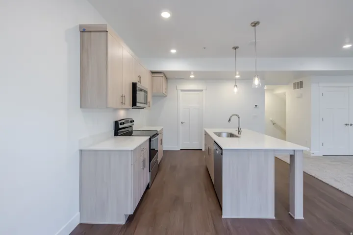 Contemporary kitchen featuring light wood-finish cabinetry, stainless steel appliances, white countertops, and wood-finish flooring