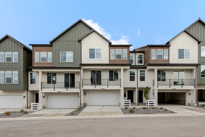 Modern townhome architecture featuring stucco and vertical siding, attached garages, and private balconies with black railings
