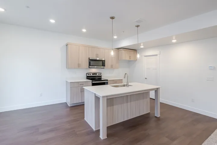 Kitchen featuring light wood-finish cabinetry, stainless steel microwave, black range, and an island with an undermount sink and pendant lighting