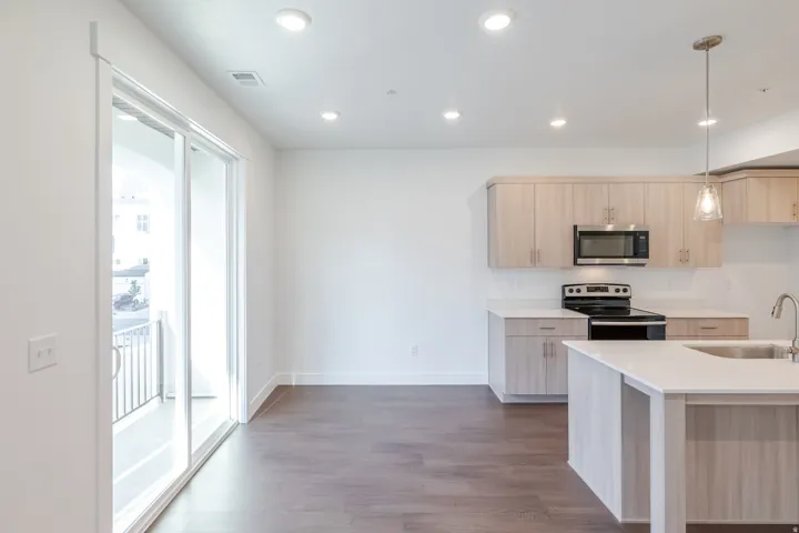 Wood-finish flooring, recessed lighting, and a kitchen island with an undermount sink, complemented by light wood-grain cabinetry and stainless steel appliances