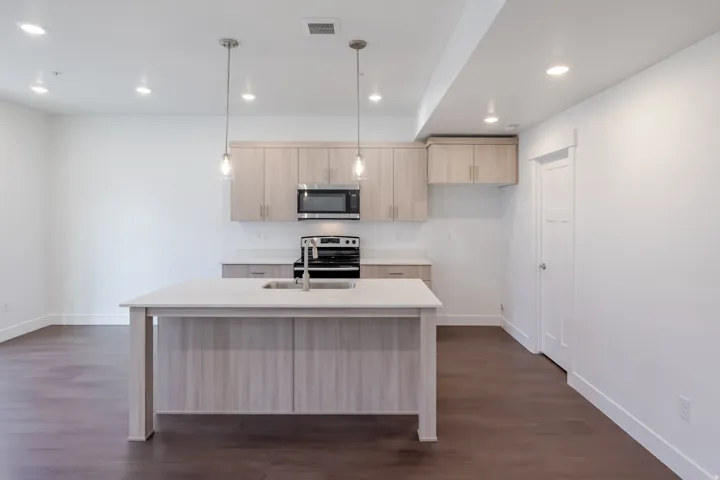 Kitchen island with an undermount sink, pendant lighting, built-in microwave, and wood-finish flooring