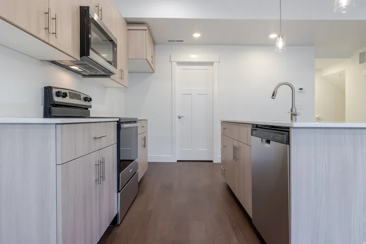 Kitchen featuring light wood-finish cabinetry, stainless steel appliances, a white countertop, and dark wood-finish flooring