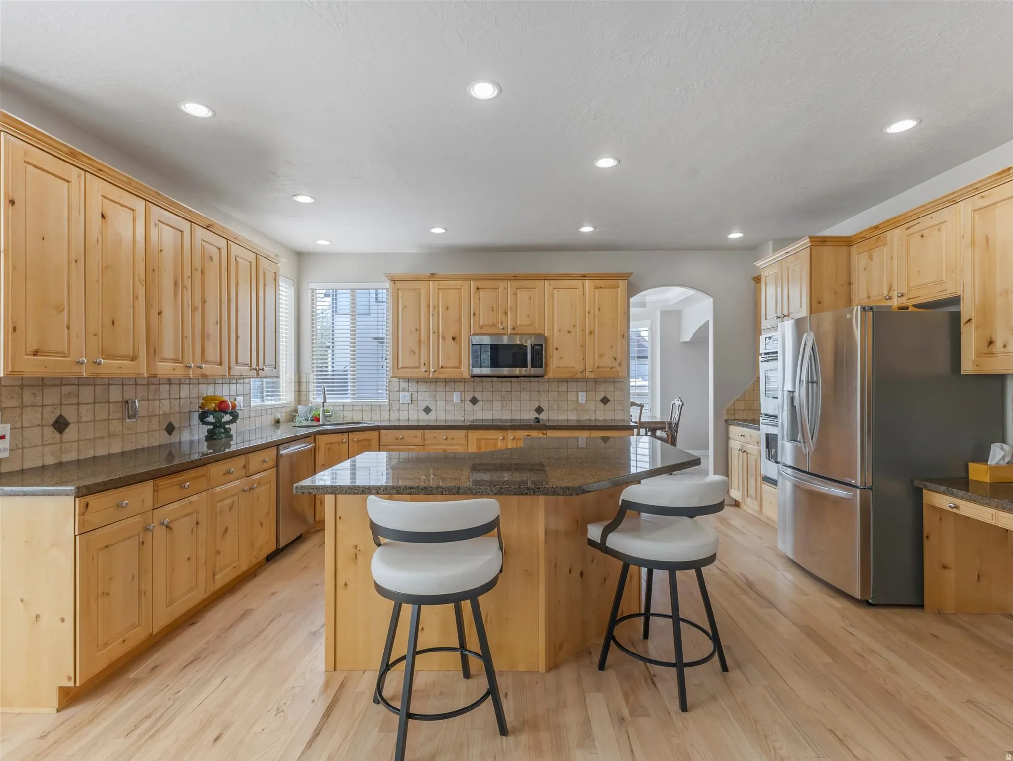 Kitchen featuring stainless steel appliances, light wood-type flooring, dark stone counters, light wood finish cabinets, and a breakfast bar area