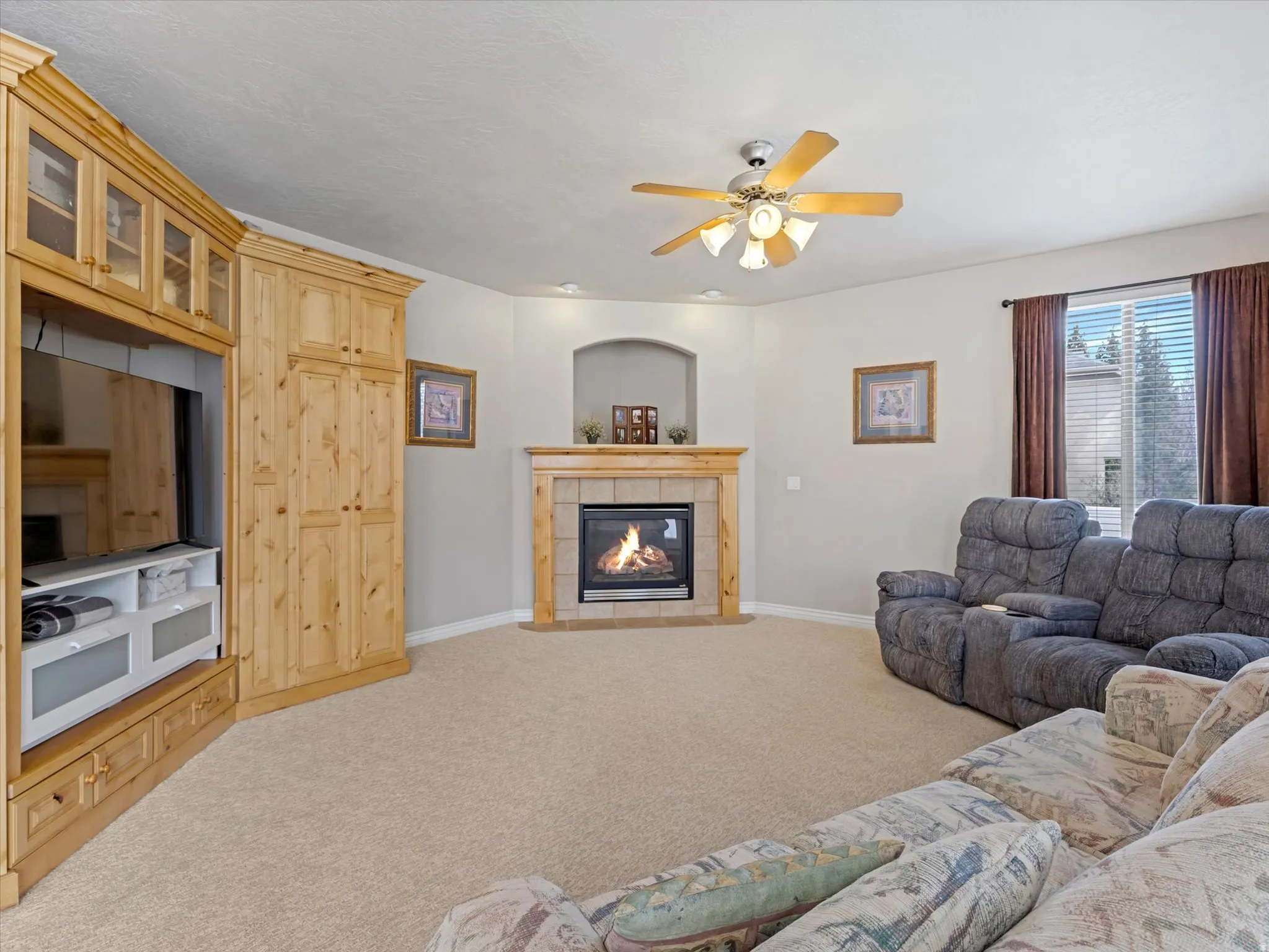 Carpeted living area with a ceiling fan and a tile fireplace