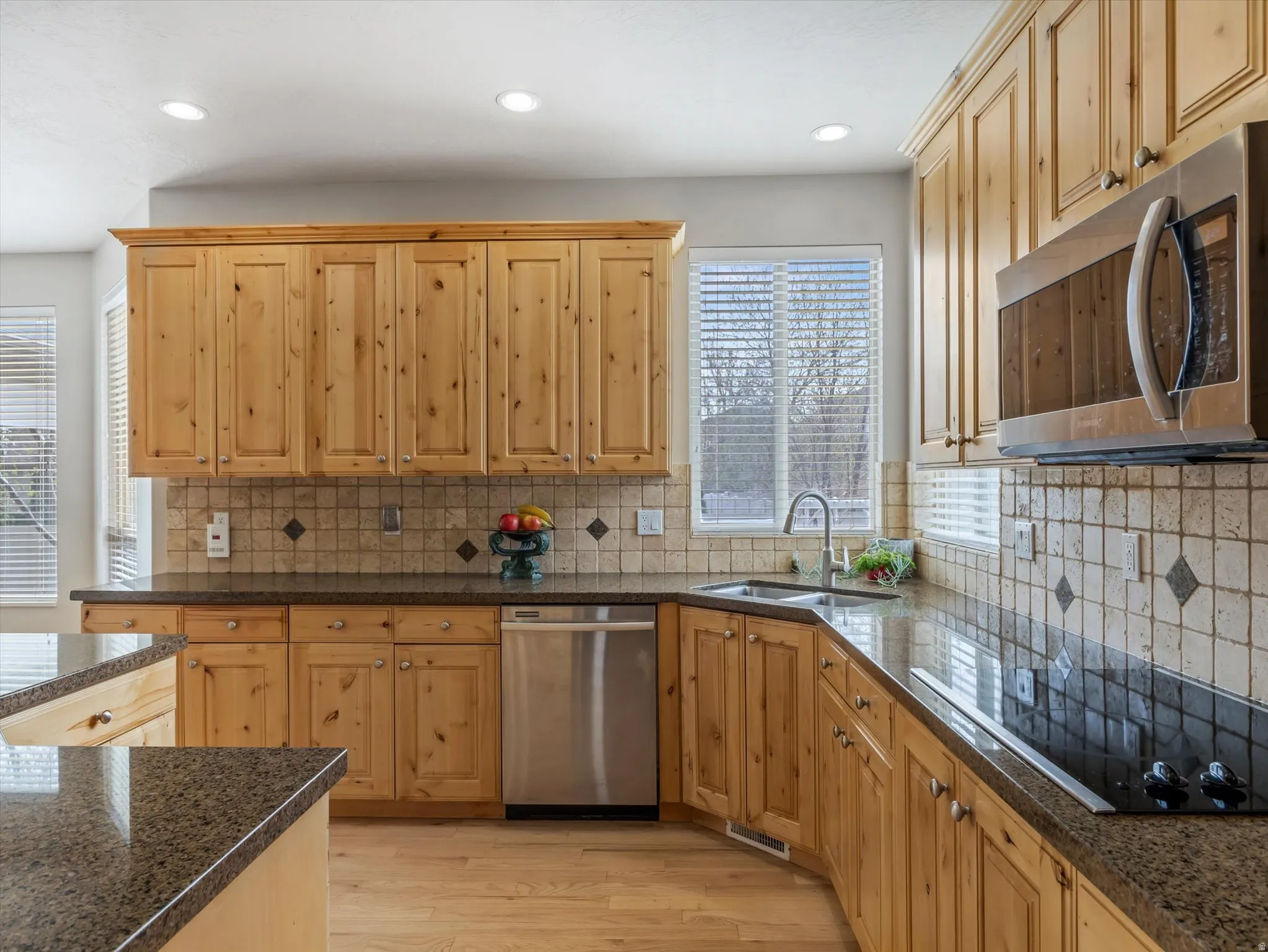 Kitchen with stainless steel appliances, light wood-type flooring, dark stone counters, tasteful backsplash, and recessed lighting