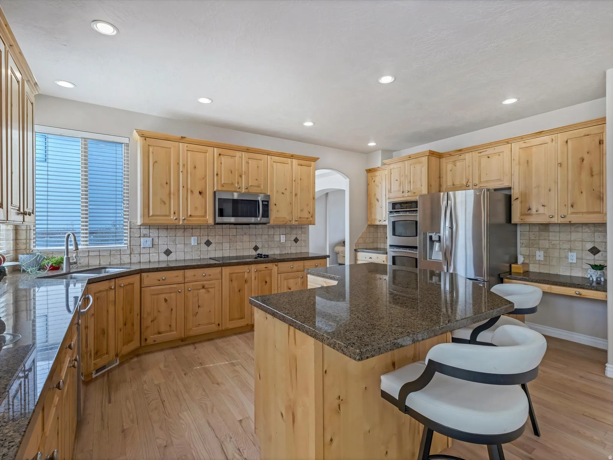 Kitchen with light wood-style floors, arched walkways, stainless steel appliances, light wood finish cabinets, and a breakfast bar