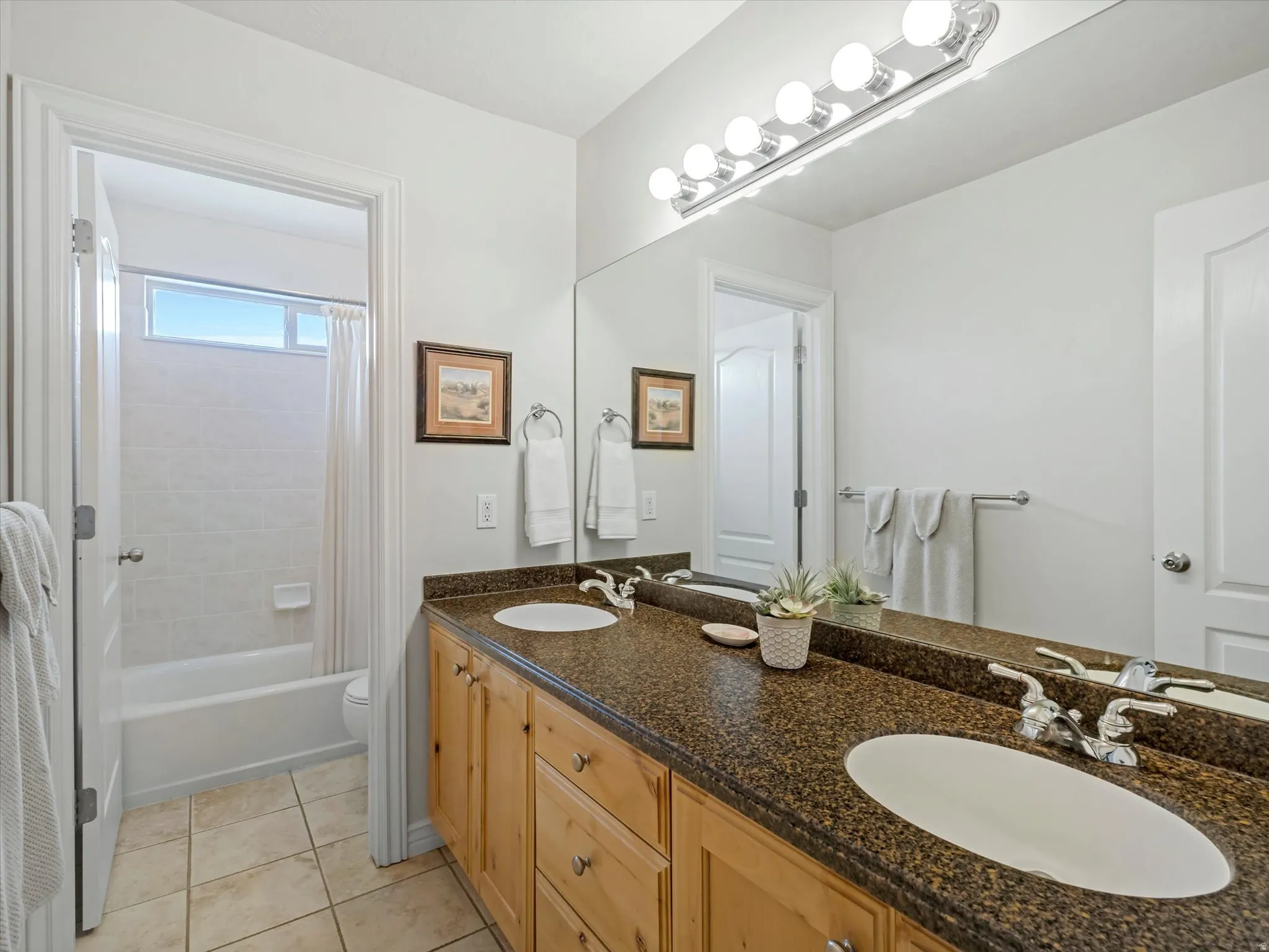Bathroom featuring double vanity, shower / bathtub combination with curtain, and light tile patterned floors