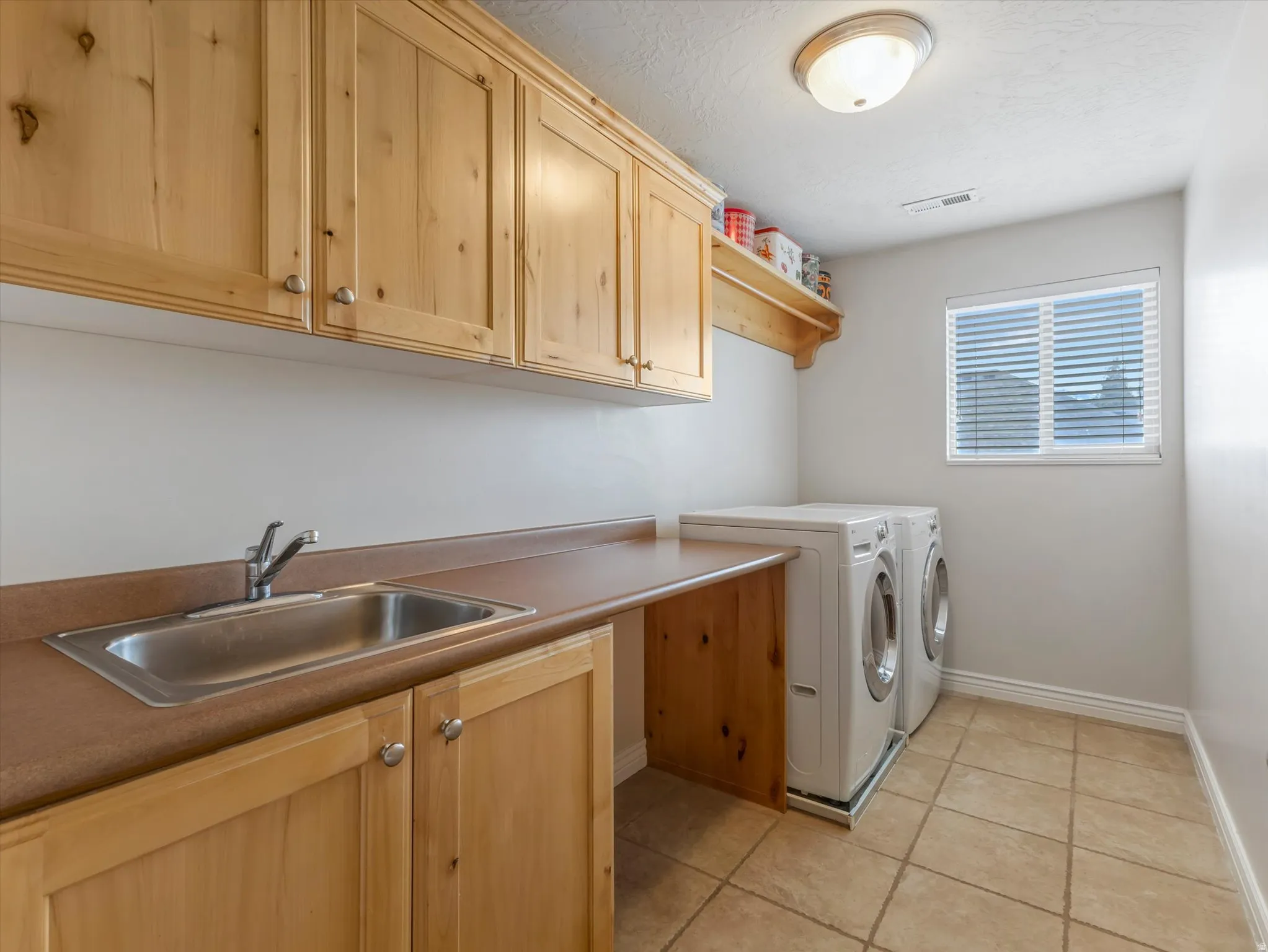 Laundry room featuring washing machine and dryer, light tile patterned floors, a textured ceiling, and cabinet space