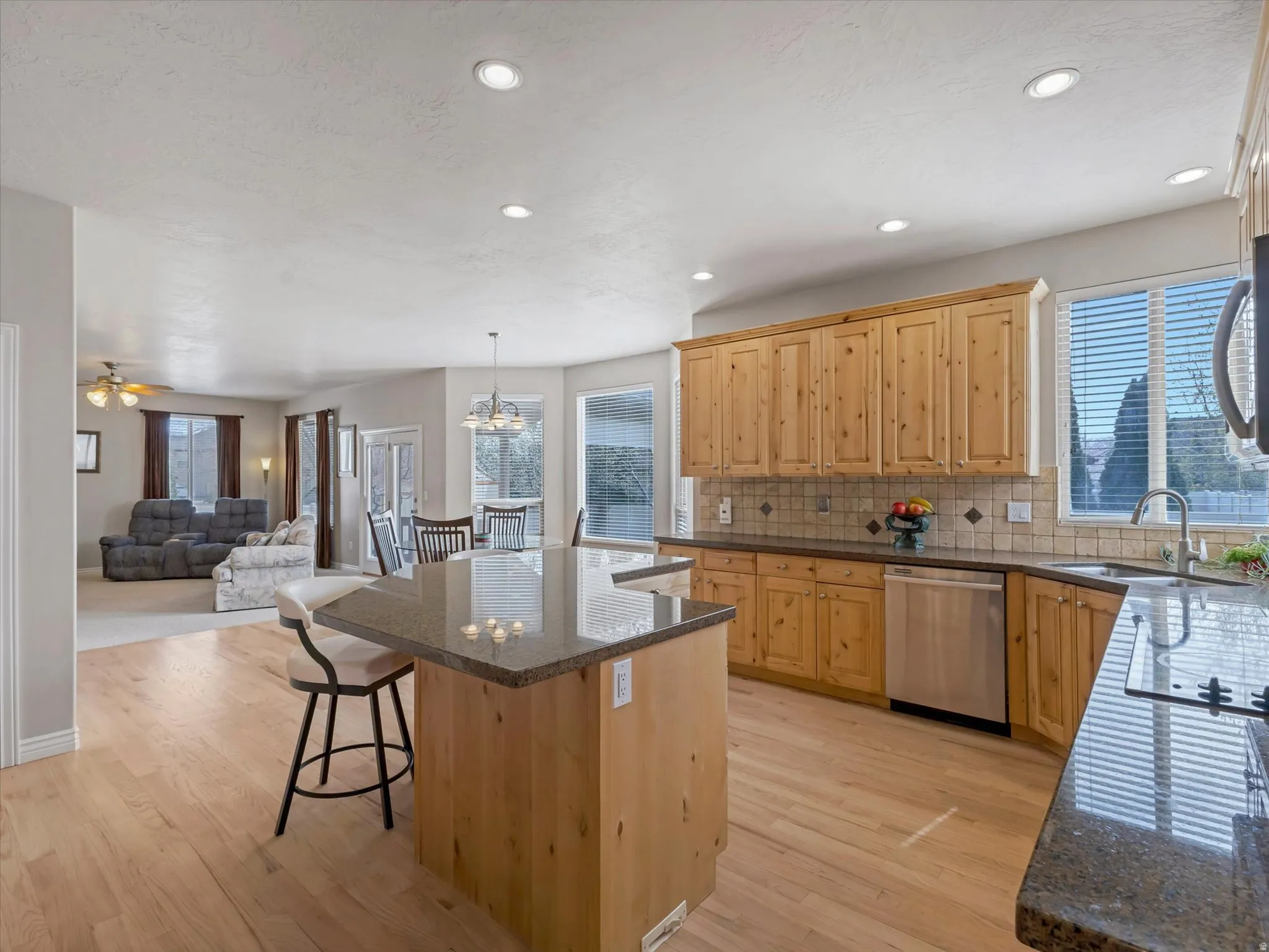 Kitchen with a kitchen island, open floor plan, light wood finish cabinets, stainless steel appliances, and ceiling fan