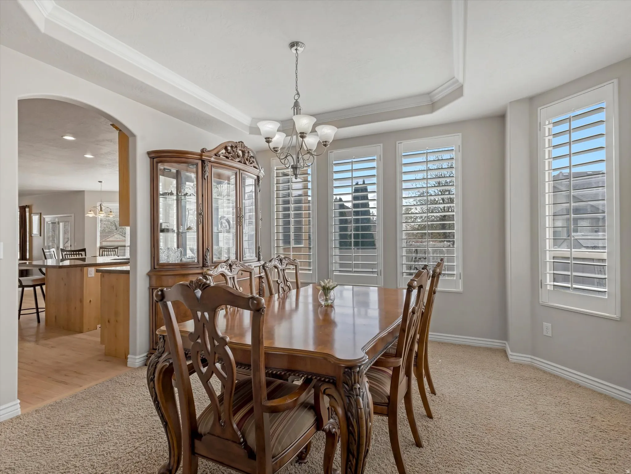 Dining space featuring suspended lighting, a tray ceiling, arched walkways, light carpet, and crown molding