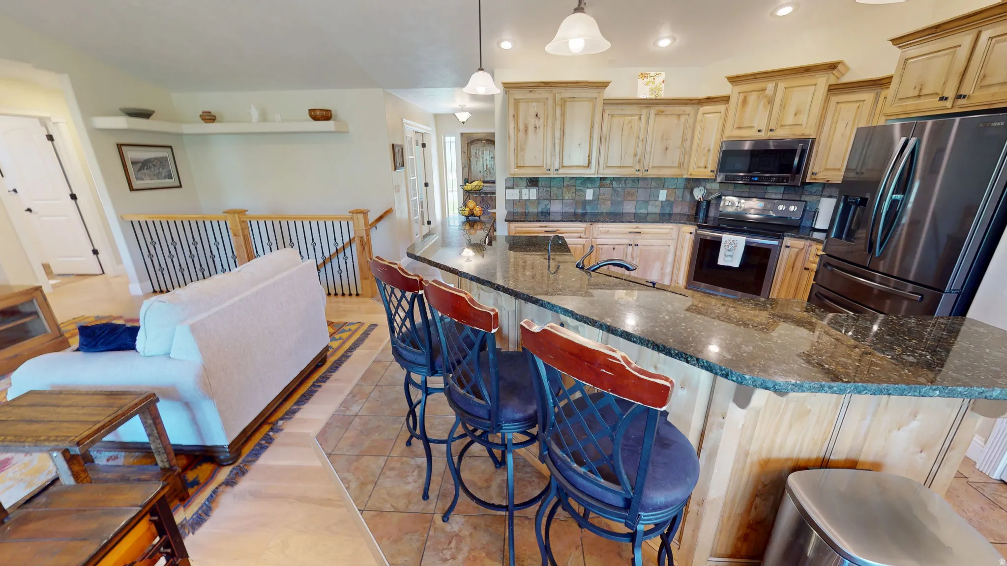 Kitchen featuring stainless steel appliances, light wood finish cabinets, backsplash, dark stone counters, and pendant lighting