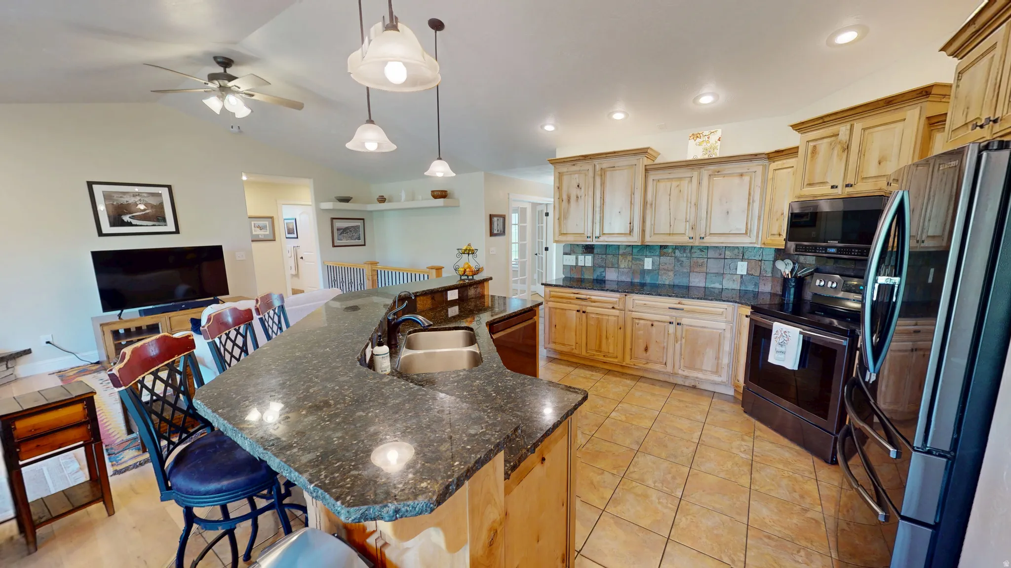 Kitchen with stainless steel appliances, light wood finish cabinetry, a kitchen bar, backsplash, and a ceiling fan