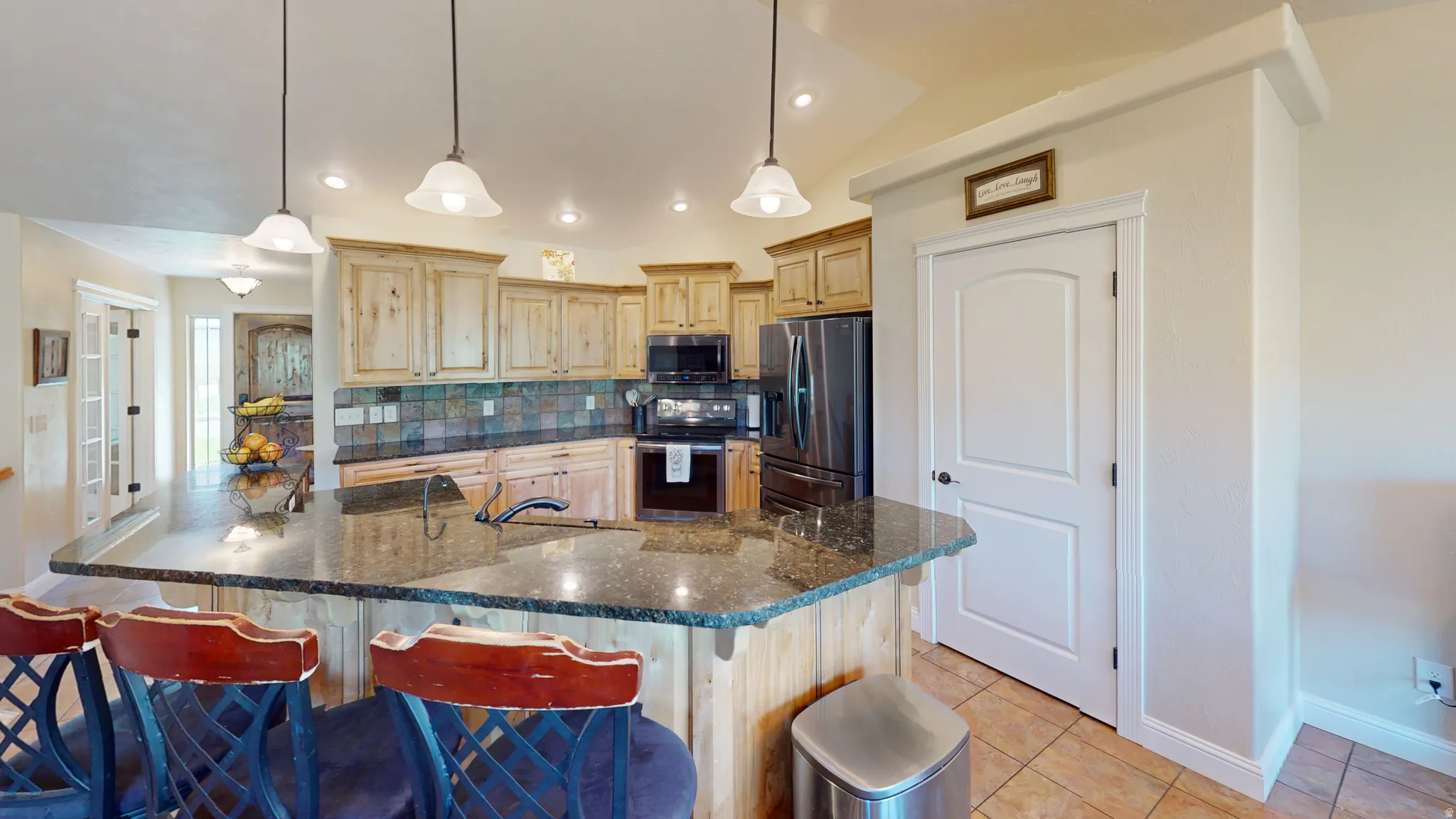 Kitchen with a breakfast bar area, stainless steel appliances, tasteful backsplash, and pendant lighting