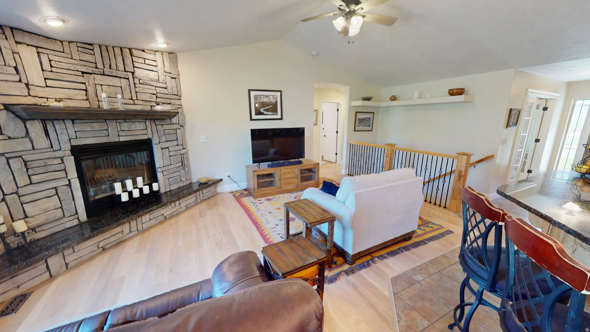Living area with ceiling fan, light wood-style floors, and a stone fireplace