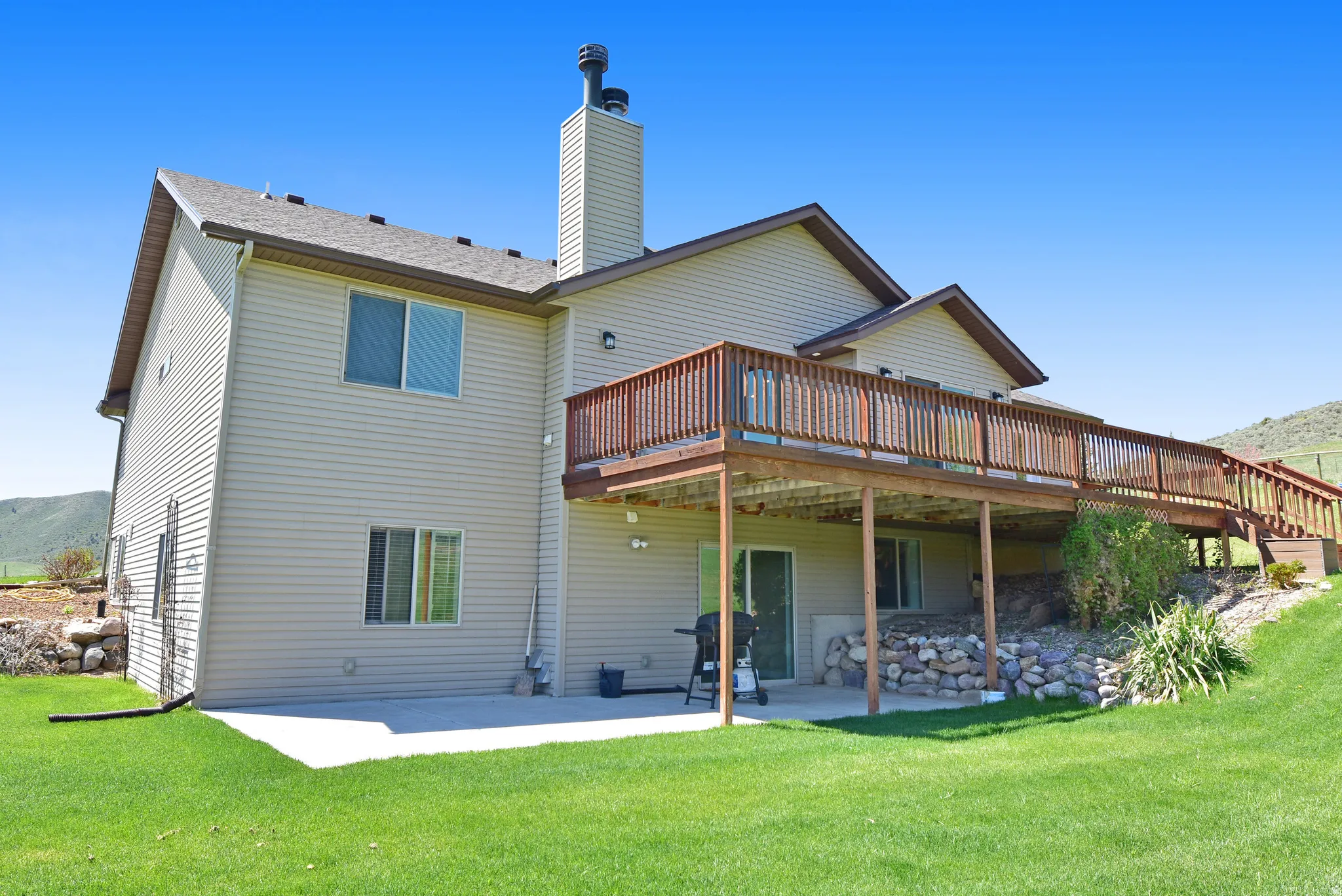 Back of house featuring a patio, a deck with mountain view, a yard, and a chimney